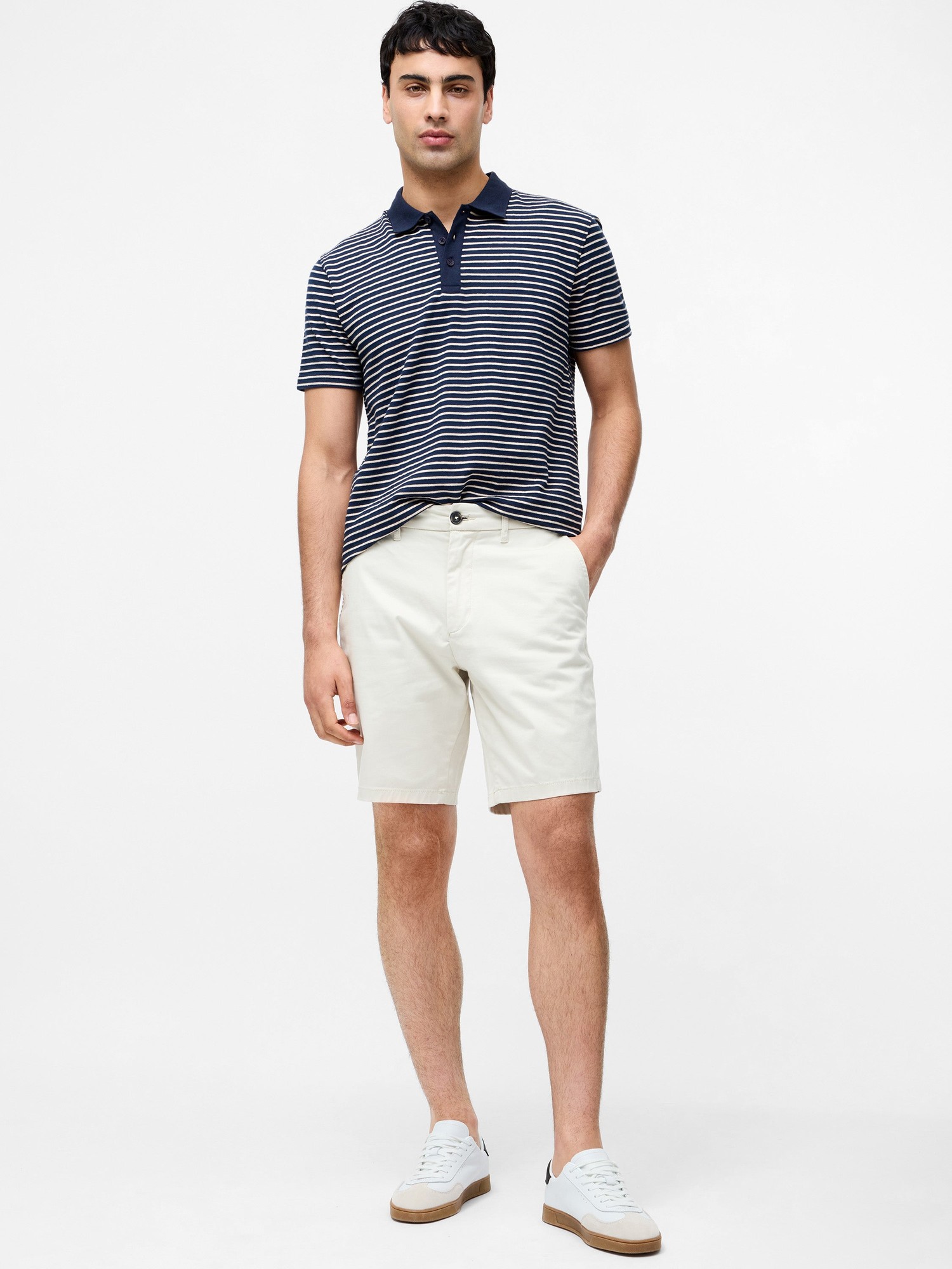 Light stone-colored cotton stretch chino shorts with a classic fit, featuring side pockets, a button closure, and styled with a navy striped polo and white sneakers.