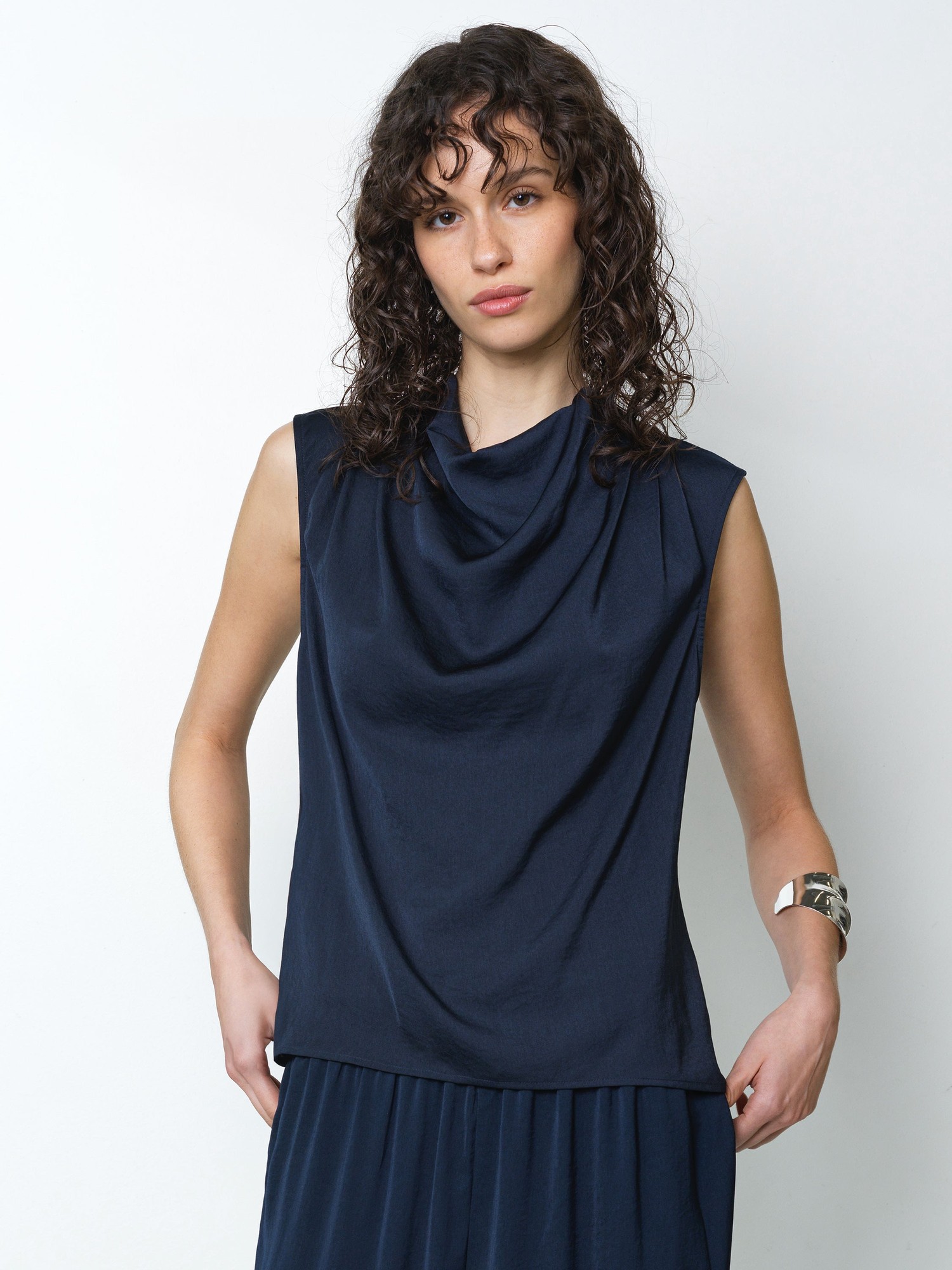 Navy sleeveless top with a draped cowl neckline and soft, lightweight fabric, featuring subtle pleats at the shoulders for added detail.