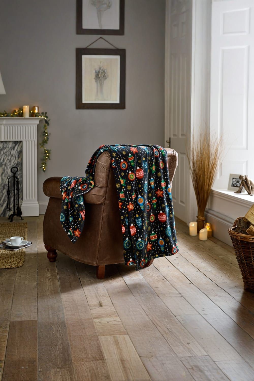 Soft navy fleece throw blanket featuring a colorful bauble print, measuring 140 x 180cm, draped over a brown armchair in a cozy, festive setting.