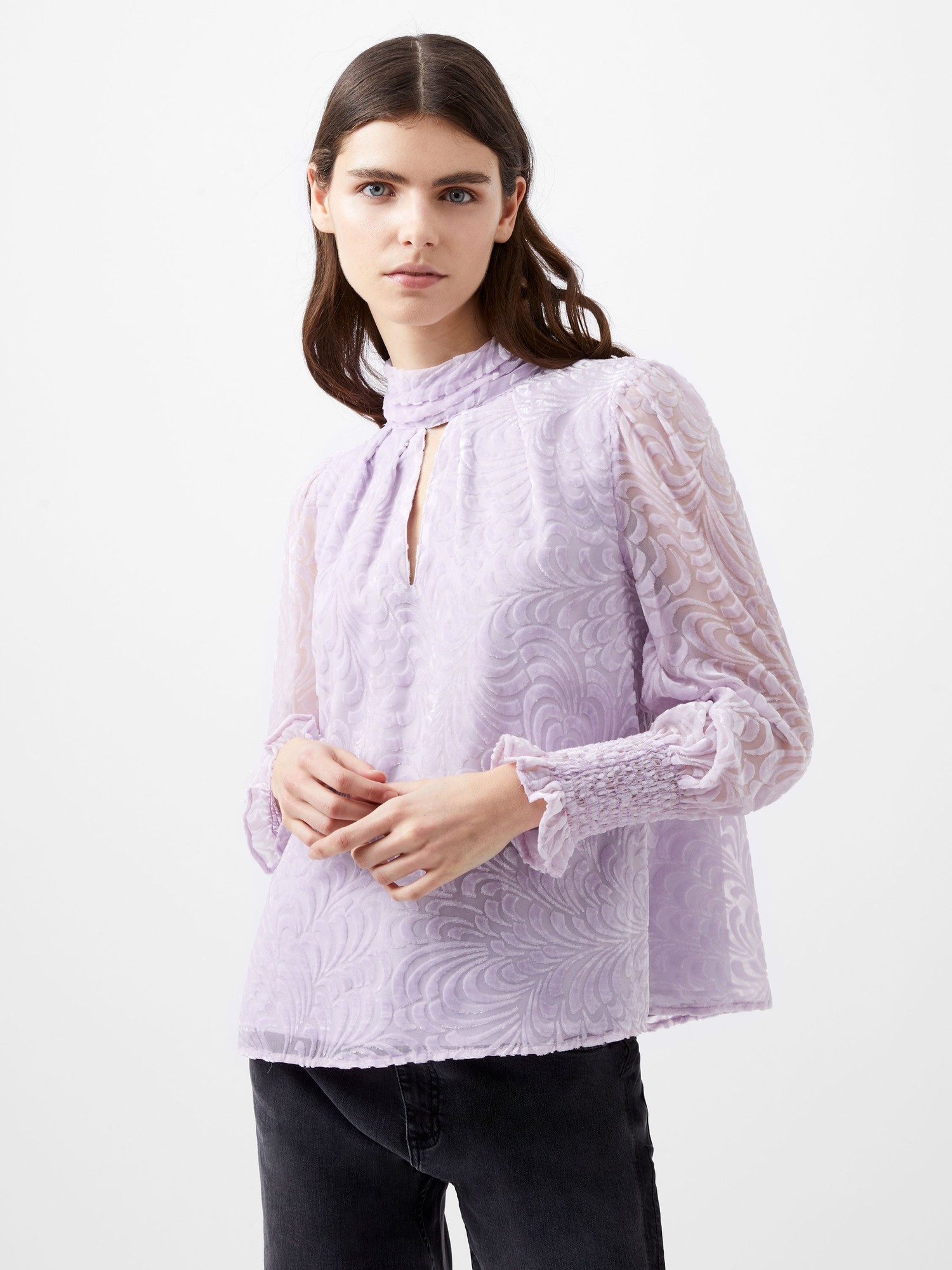 Light lavender long sleeve high neck top with textured floral pattern, featuring a keyhole opening and smocked cuffs, styled with black jeans.