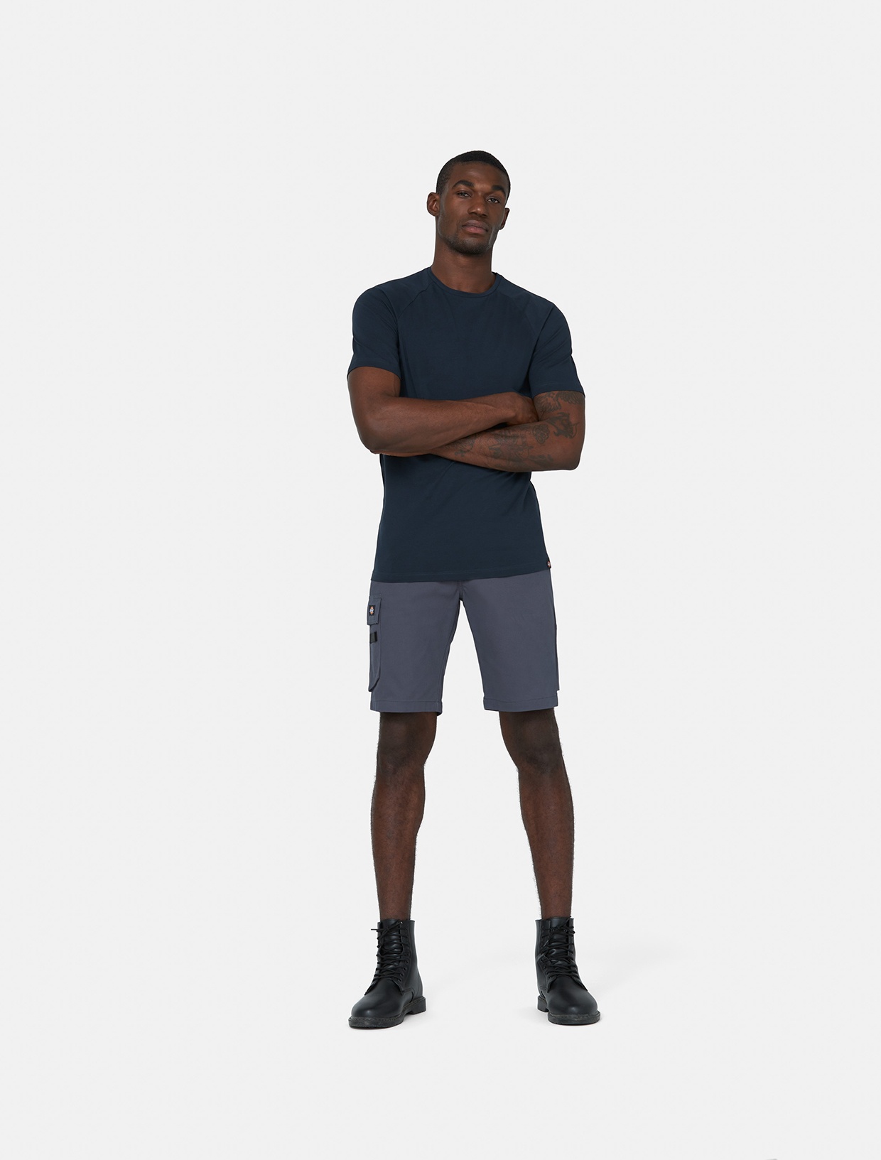 Grey knee-length shorts made of polyester, featuring a side cargo pocket, paired with a fitted navy t-shirt and black boots, worn by a standing male model.