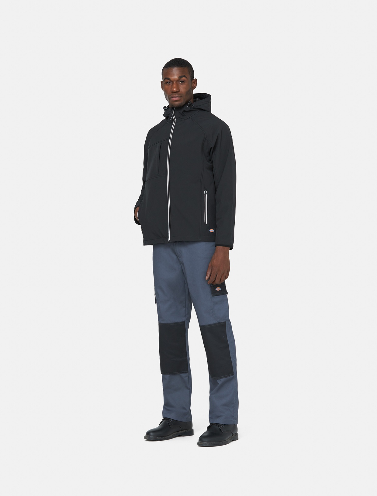Men's grey outdoor trousers made of polyester, featuring cargo pockets and contrasting black knee panels, paired with a black jacket and black shoes.