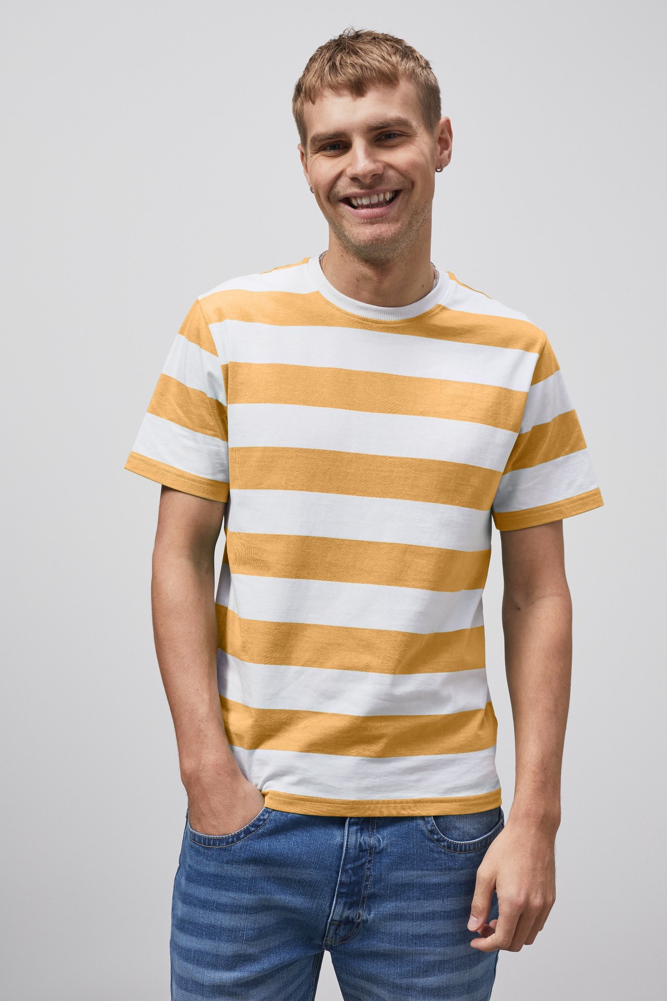 Yellow and white striped short-sleeve t-shirt made of cotton, featuring a crew neckline, worn by a smiling man with hands in pockets, paired with blue jeans.