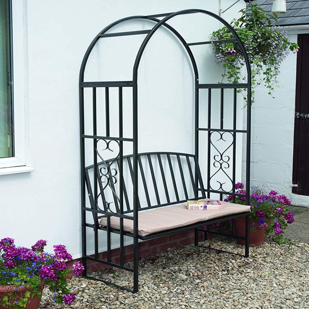 Black metal rose arch trellis with a curved top and decorative side panels, featuring a built-in bench with a light-colored cushion, surrounded by potted flowers.