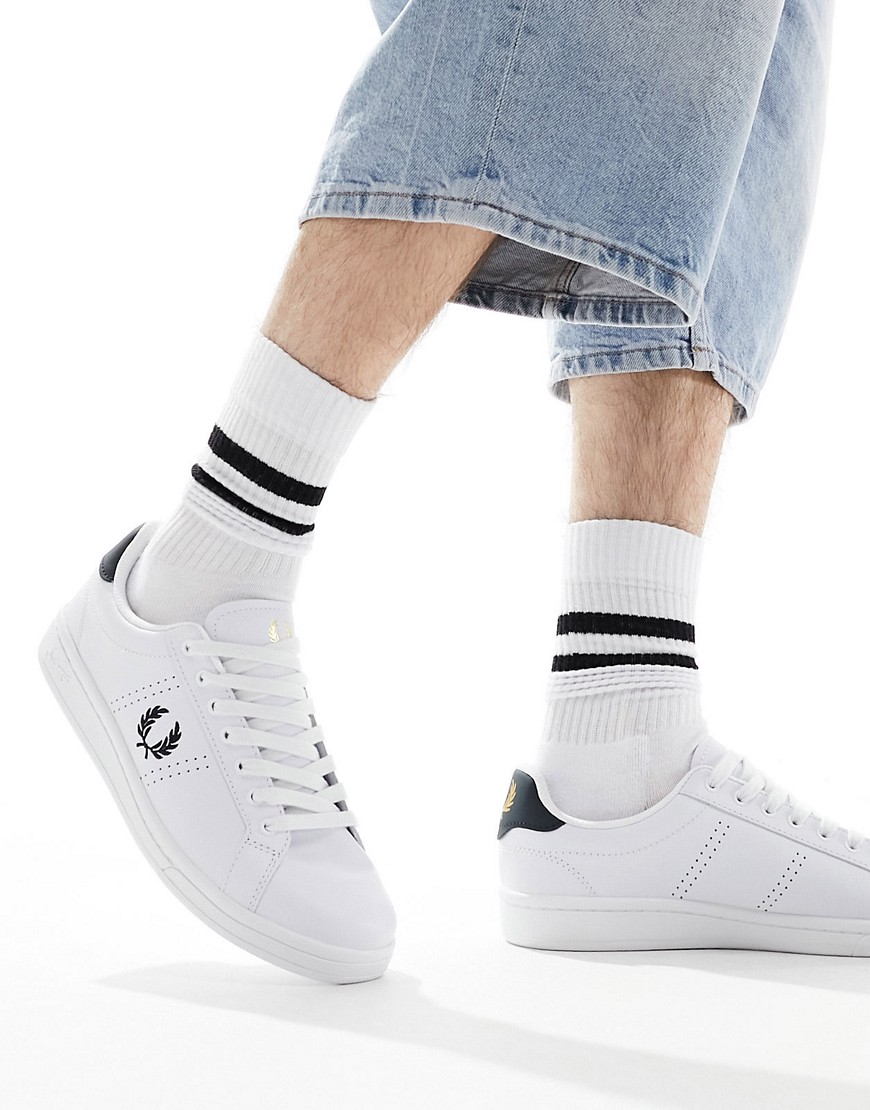 White leather trainers with a navy heel tab, featuring the iconic Fred Perry laurel logo, paired with cropped denim and striped white socks.