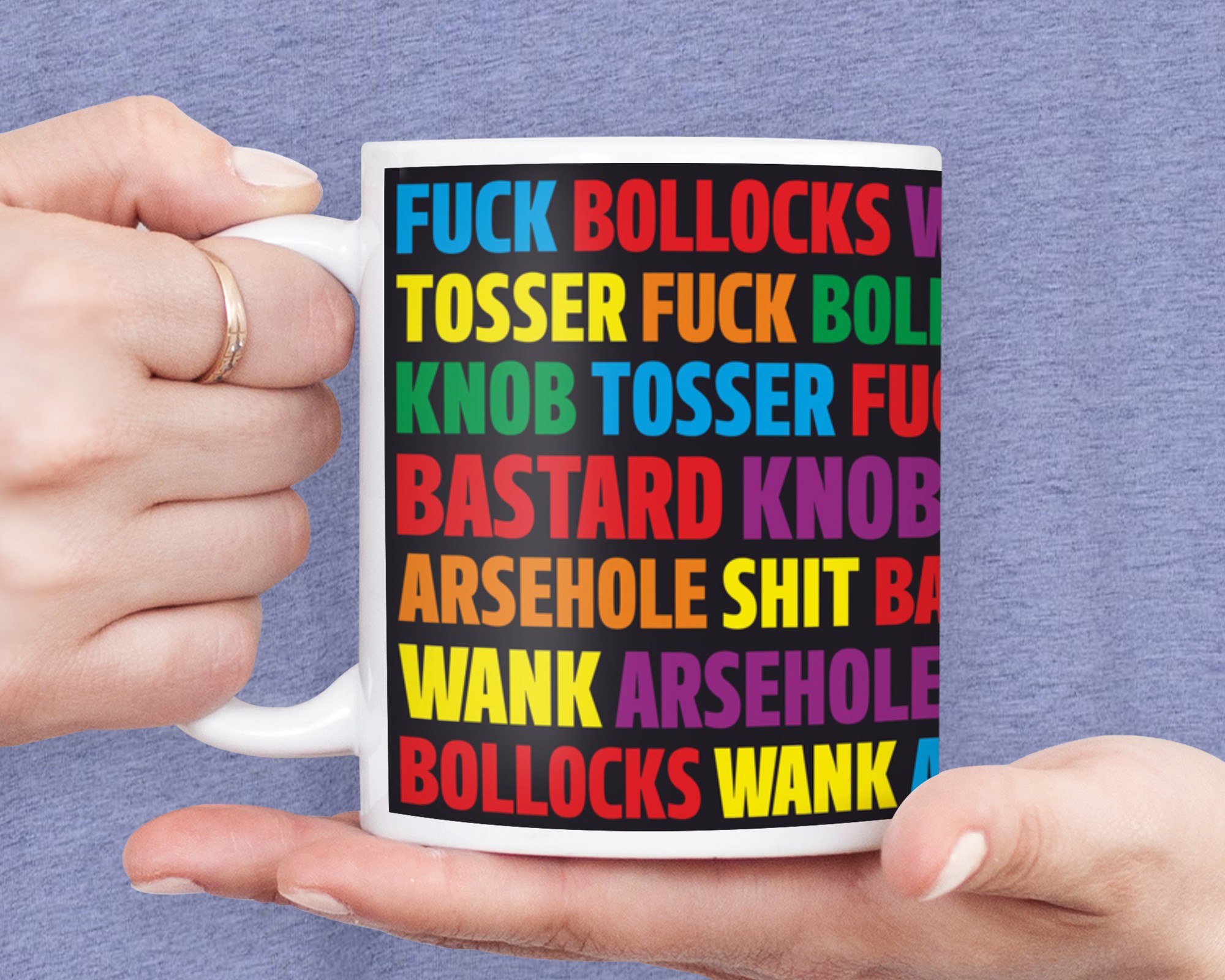 White ceramic mug held by a hand, featuring a colorful design with bold, repeated text in various colors that includes profanity and humorous phrases.