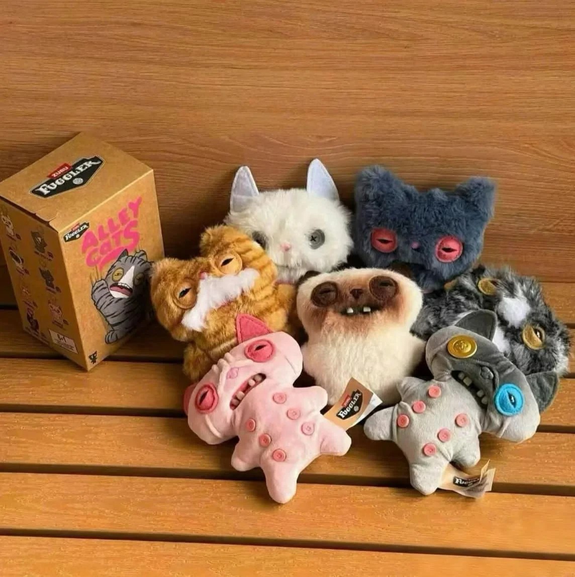 Colorful plush keyrings of quirky, funny monsters with distinct facial features, including oversized eyes and unique textures, displayed around a Fuggler Alley Cats blind box.