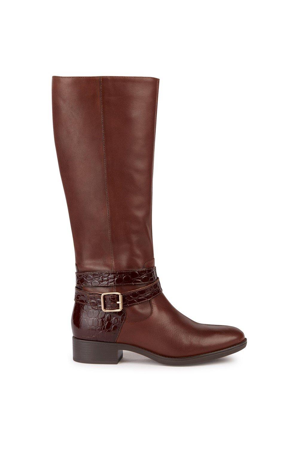 Brown leather knee-high boots featuring a textured croc-embossed strap with a buckle, and a low block heel for added comfort.