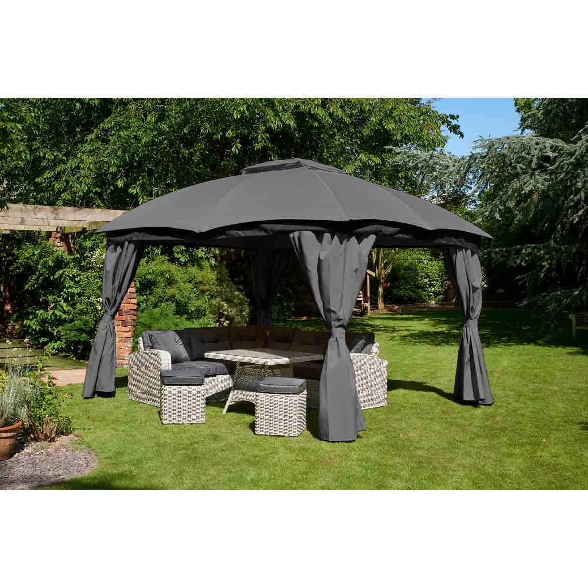 Grey Glendale Rio Gazebo measuring 3x3.65m features a sturdy frame, fabric canopy, and flowing curtains, set over a wicker seating area in a lush garden.