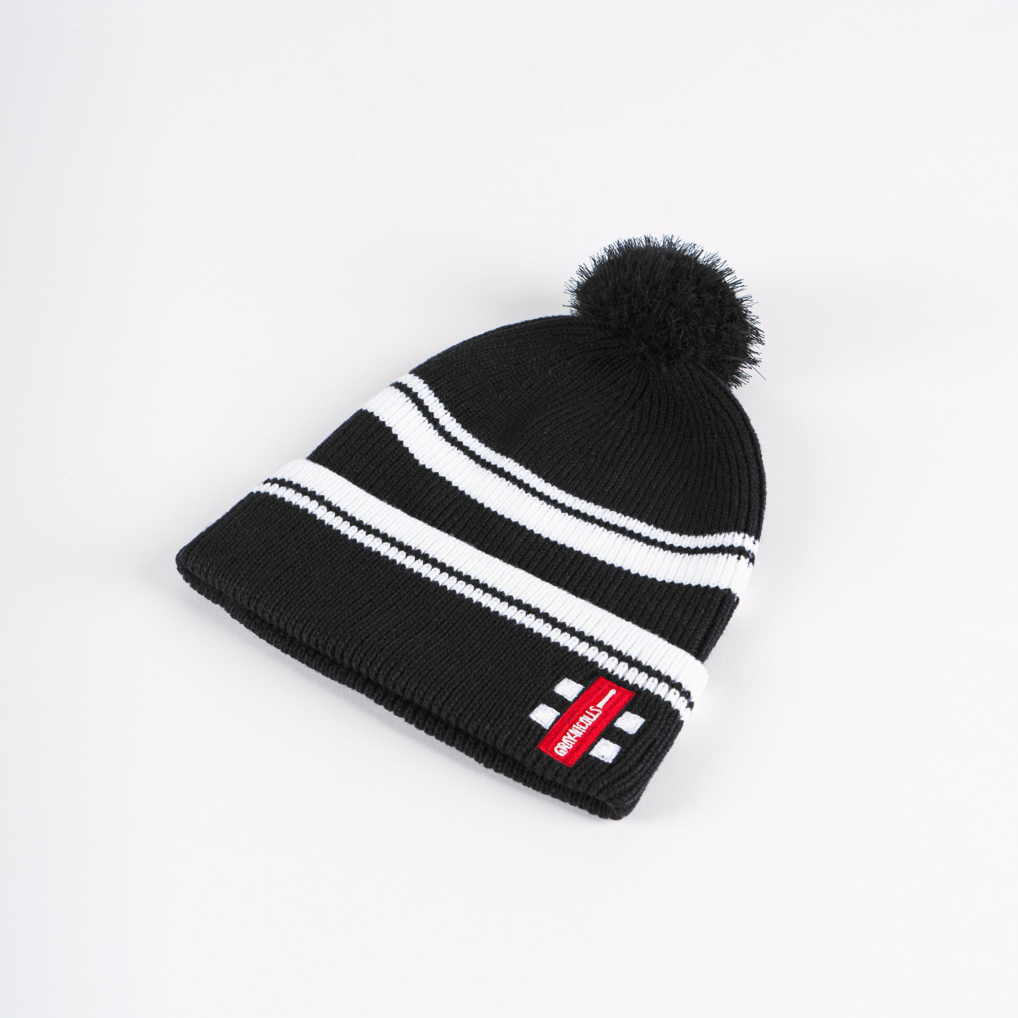 Black knitted bobble hat featuring white stripes and a pom-pom on top, with a small red Gray-Nicolls logo tag on the side.