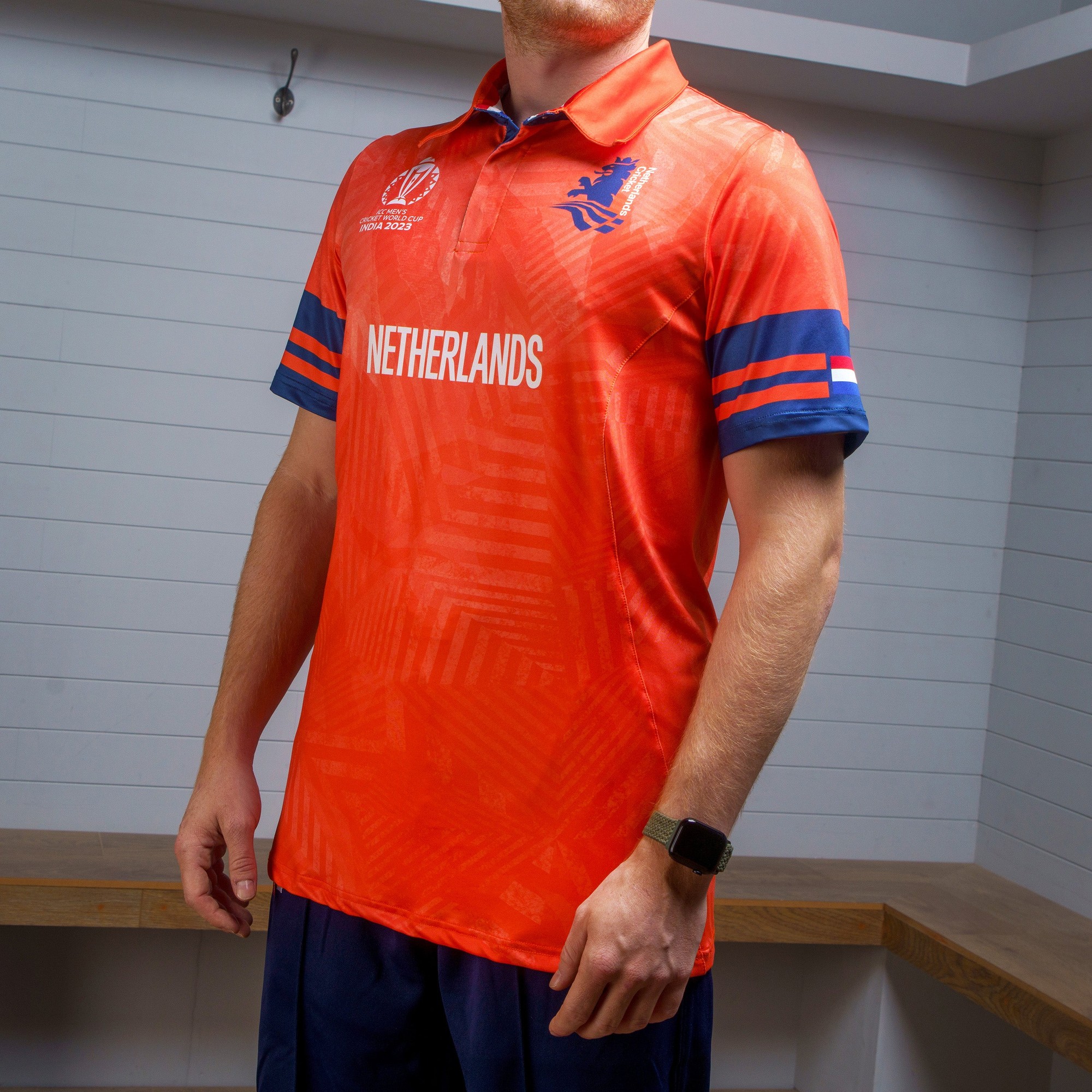 Bright orange short-sleeve cricket shirt with blue accents, featuring "NETHERLANDS" printed prominently, and the Netherlands national emblem on the chest.