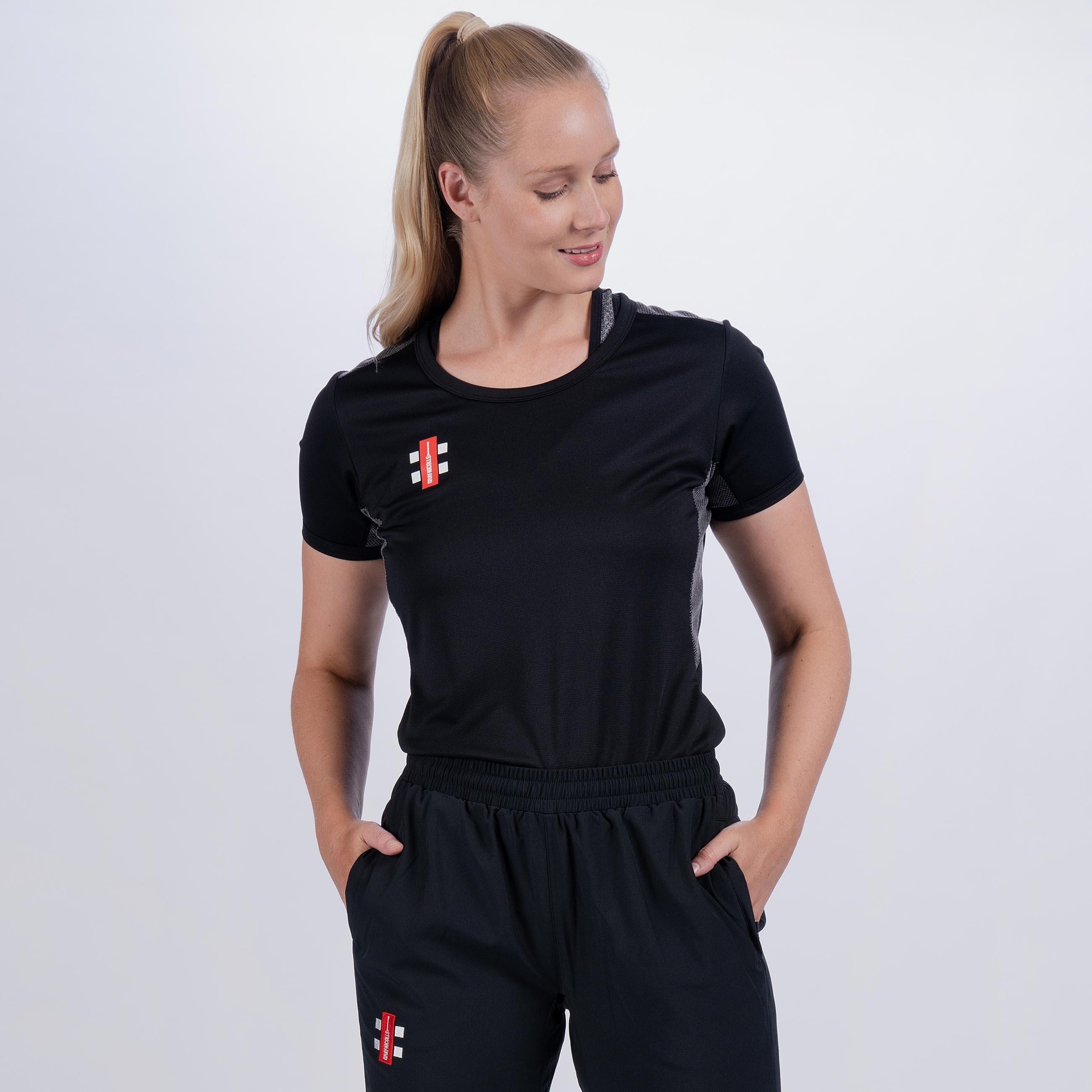 Black short sleeve women's t-shirt by Gray-Nicolls, featuring a round neckline, lightweight fabric, and a small logo on the chest, styled with matching black athletic pants.