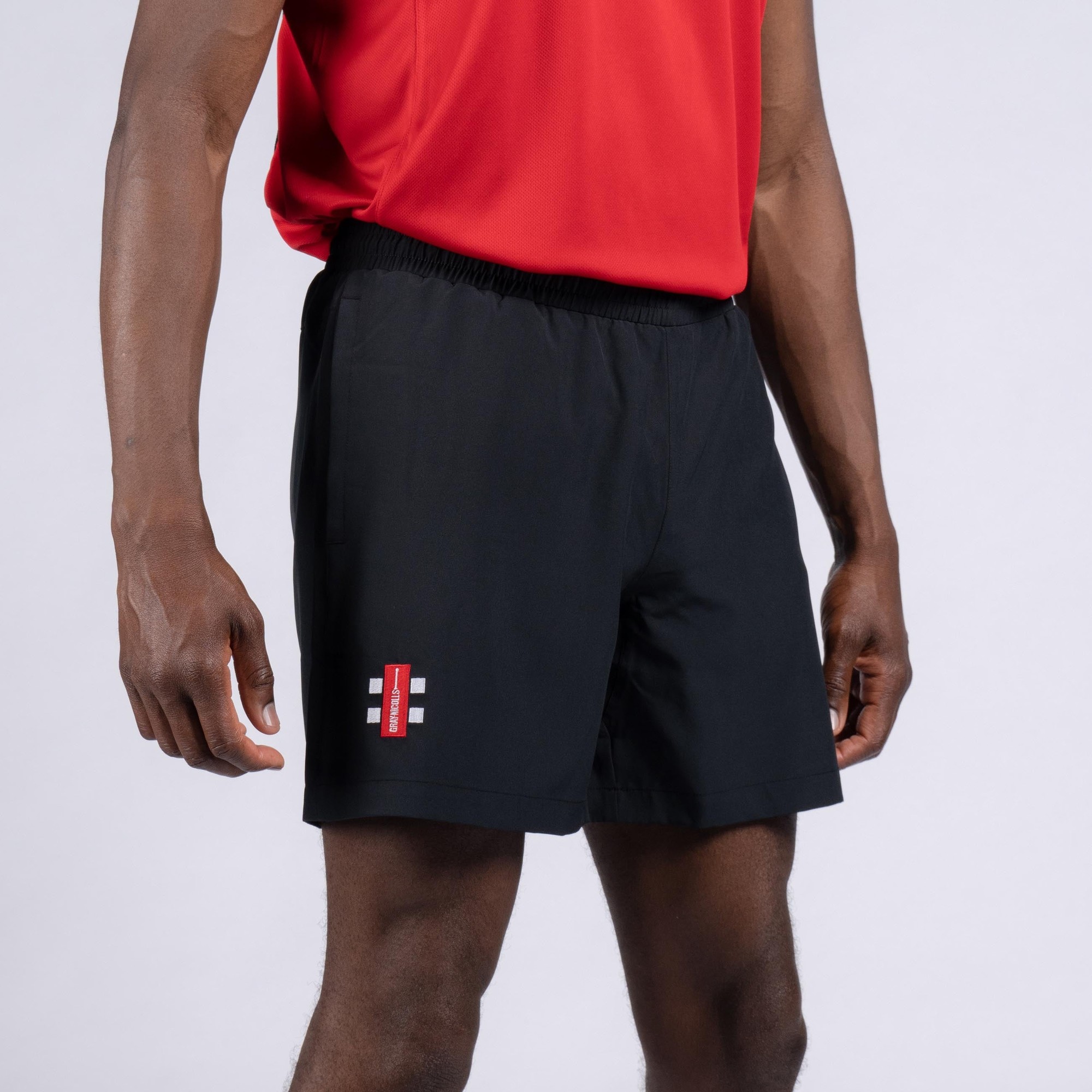 Black junior shorts by Gray-Nicolls with an elastic waistband, featuring a red and white logo on the left leg, made from lightweight, breathable material.
