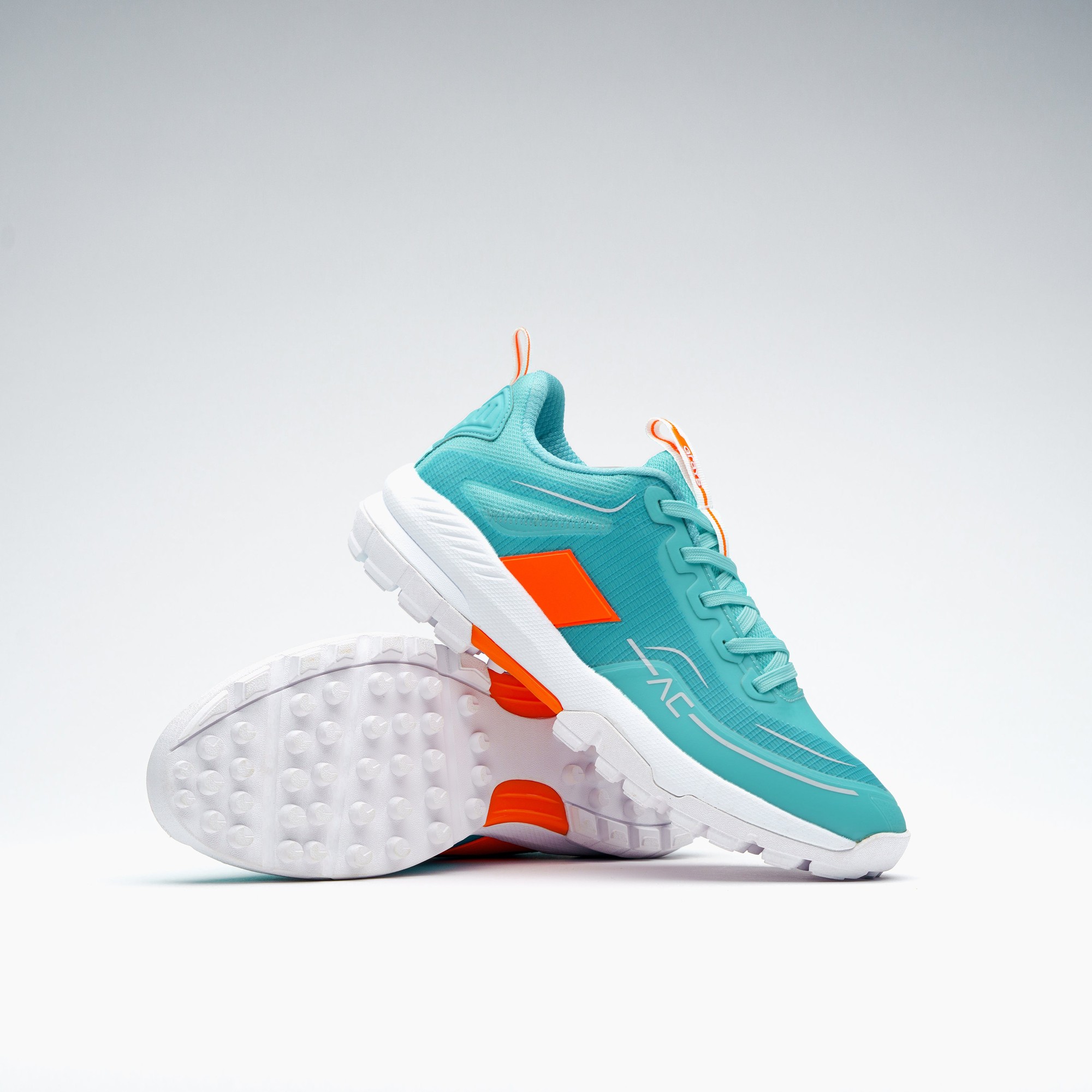 Teal junior hockey shoes featuring a breathable mesh upper, vibrant orange accents, and a textured white rubber sole for enhanced grip and comfort.