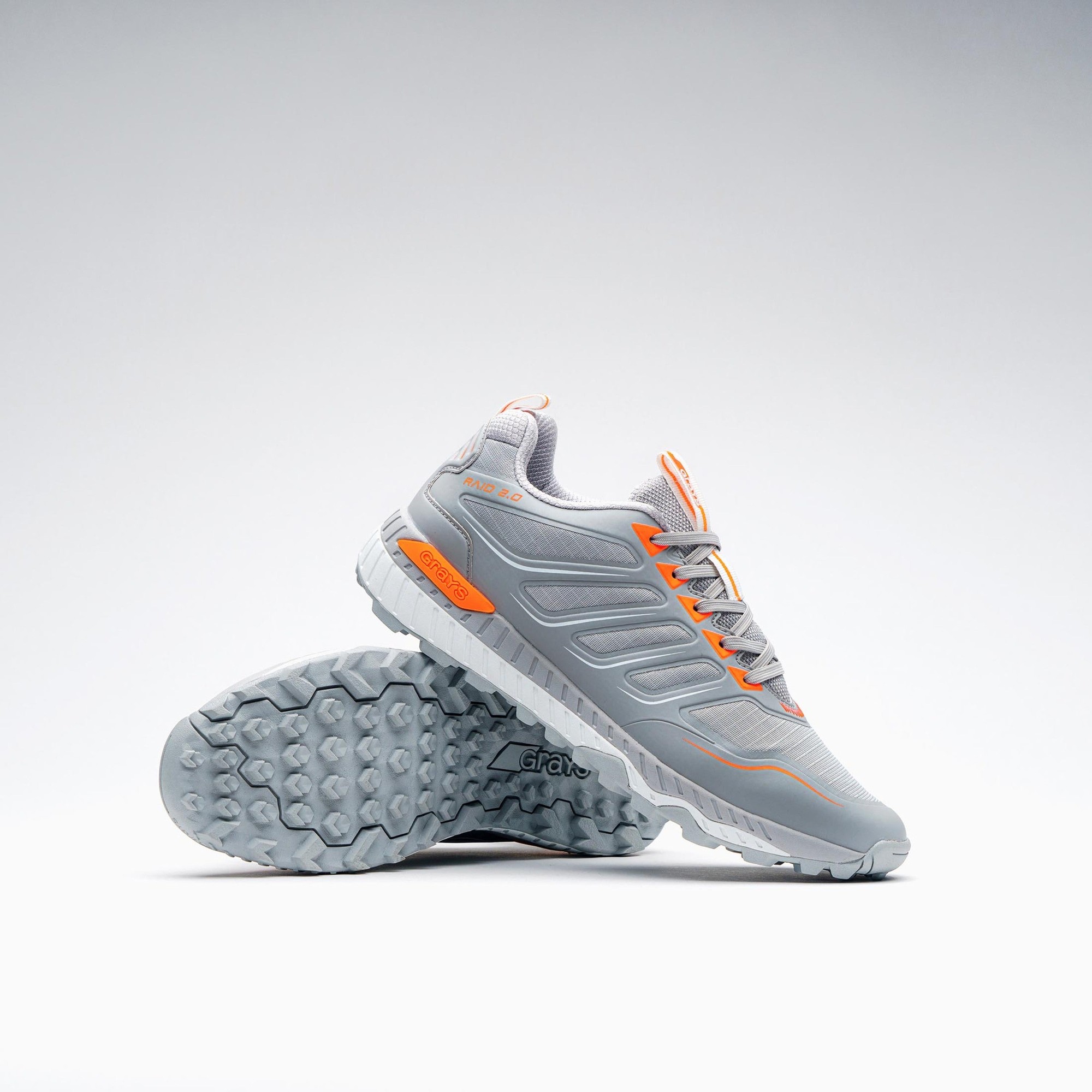 Light gray junior hockey shoes with orange accents, featuring a textured sole for grip and a cushioned design for comfort, ideal for young athletes.