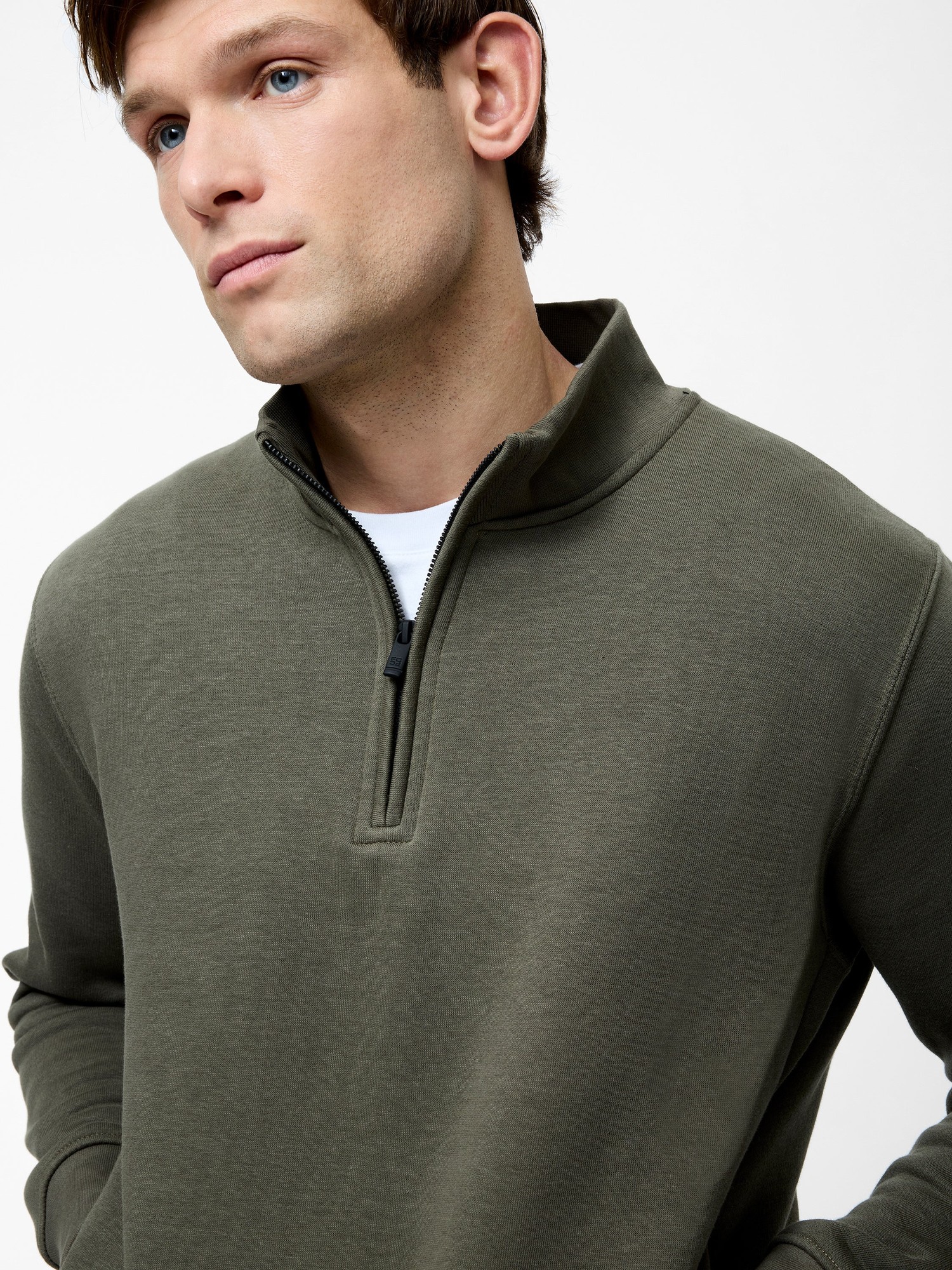 Olive green half zip funnel neck sweatshirt made of soft material, featuring a zip closure and a relaxed fit, styled with a white t-shirt underneath.