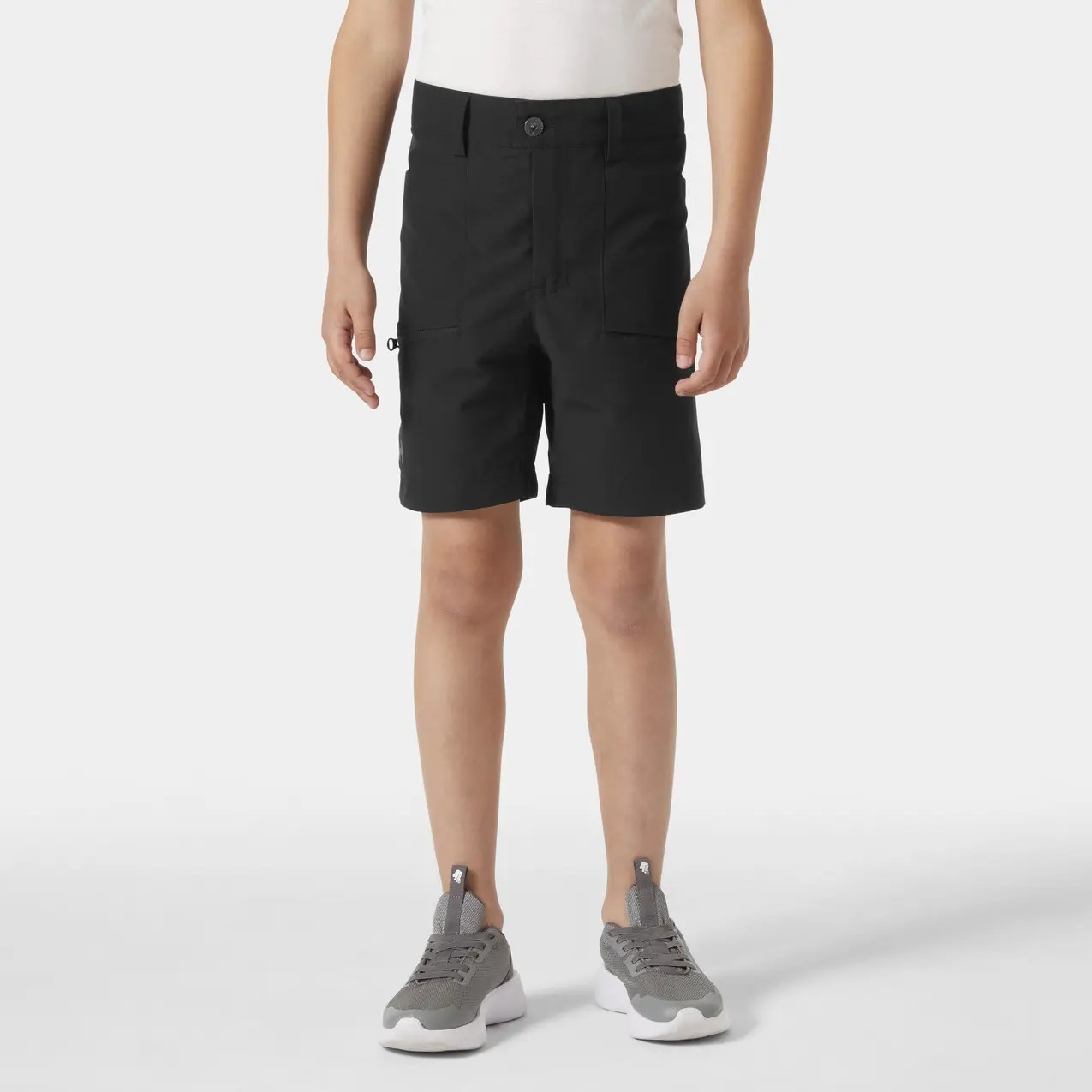 Black children's shorts by Helly Hansen, featuring a zippered pocket, belt loops, and a classic fit, paired with a white shirt and gray sneakers.