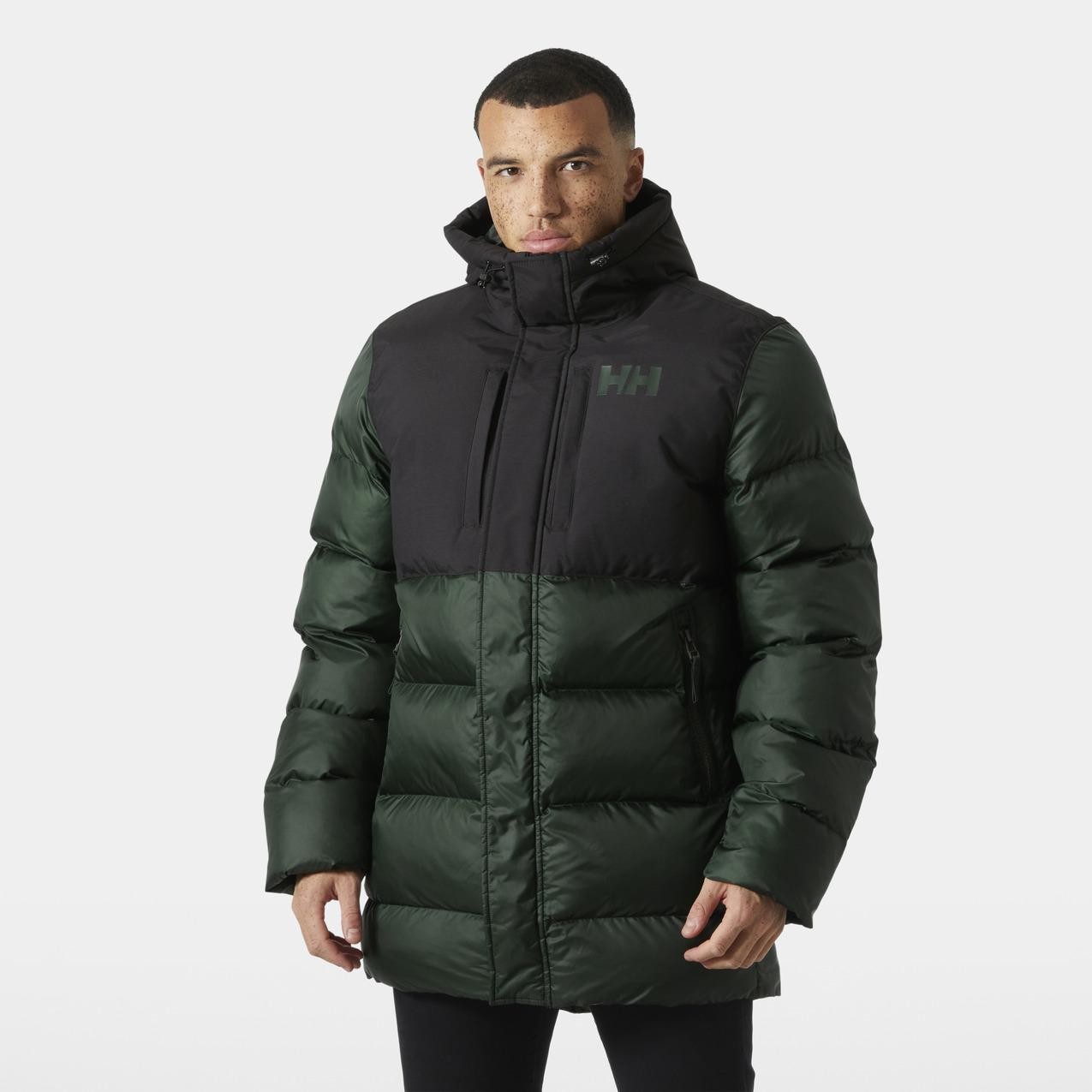 Long hooded down jacket featuring a black upper section and dark green lower section, made from shiny, insulated material, with a zippered front and Helly Hansen logo on the chest.