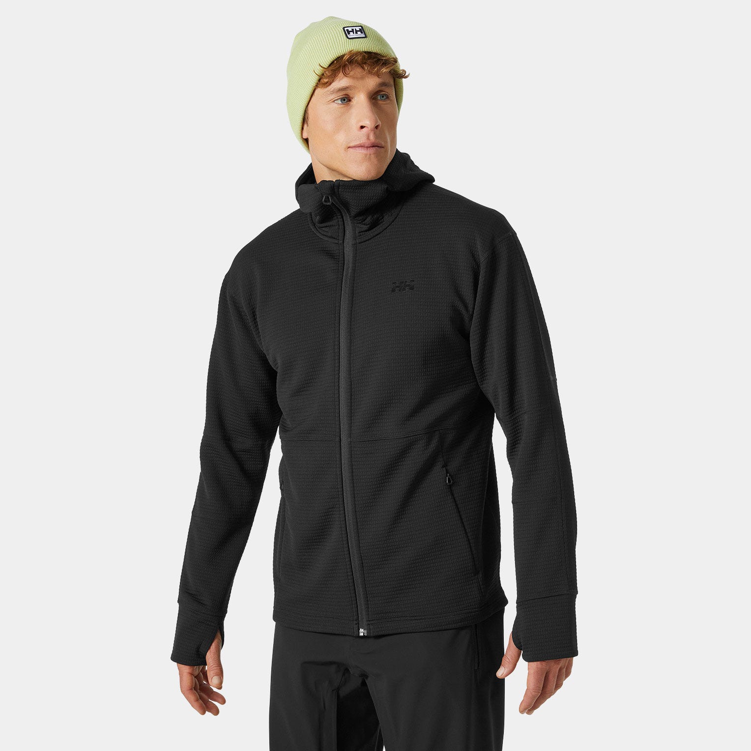 Black hooded sweatshirt by Helly Hansen featuring a textured fabric, full zip, and a fitted design, complemented by a light green beanie.