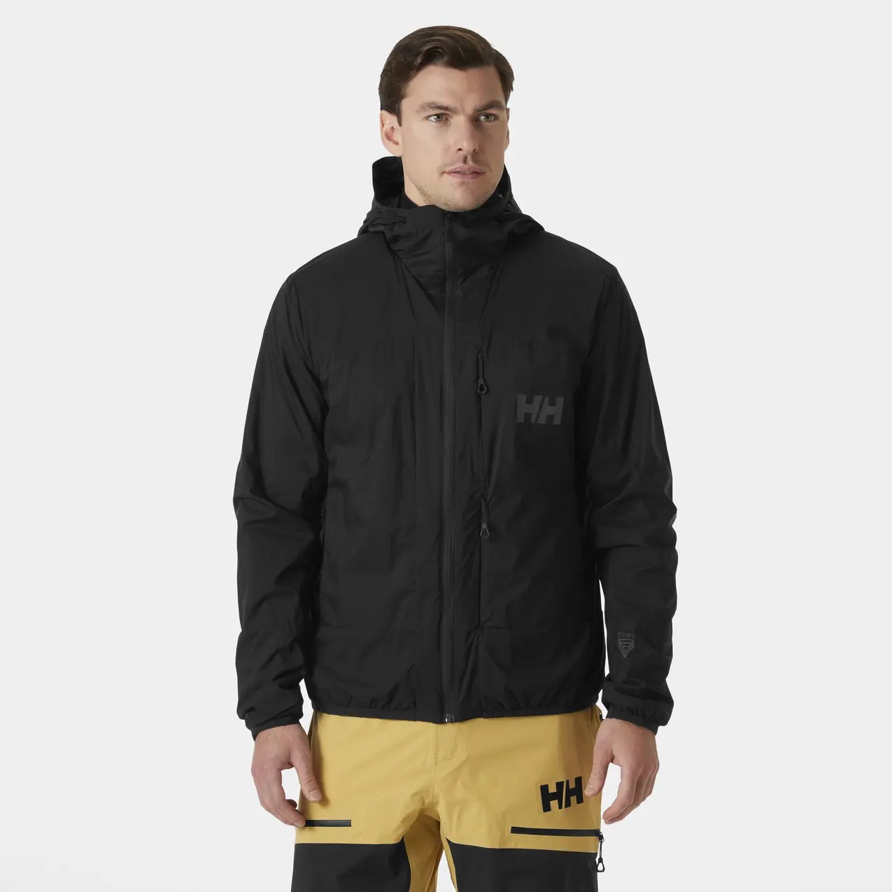Black insulated waterproof hooded jacket featuring a zippered front, adjustable cuffs, and the Helly Hansen logo on the chest, paired with yellow ski pants.