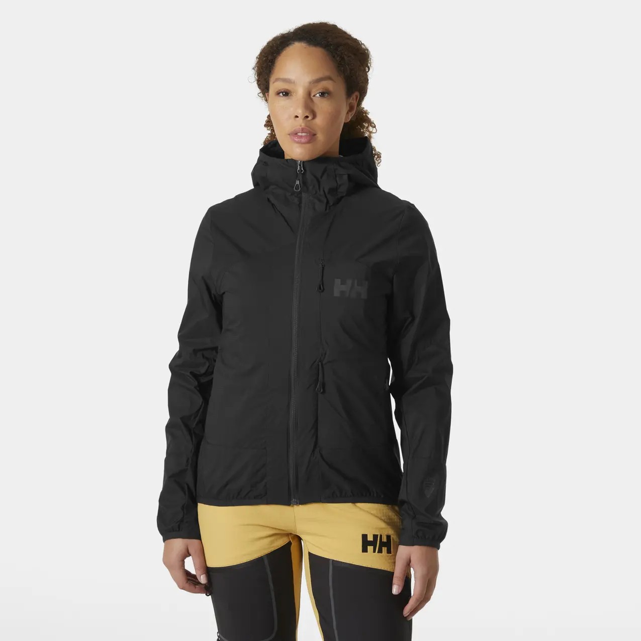 Black women's hooded waterproof jacket by Helly Hansen, featuring a zip front, adjustable hood, and logo on the chest, paired with yellow athletic pants.