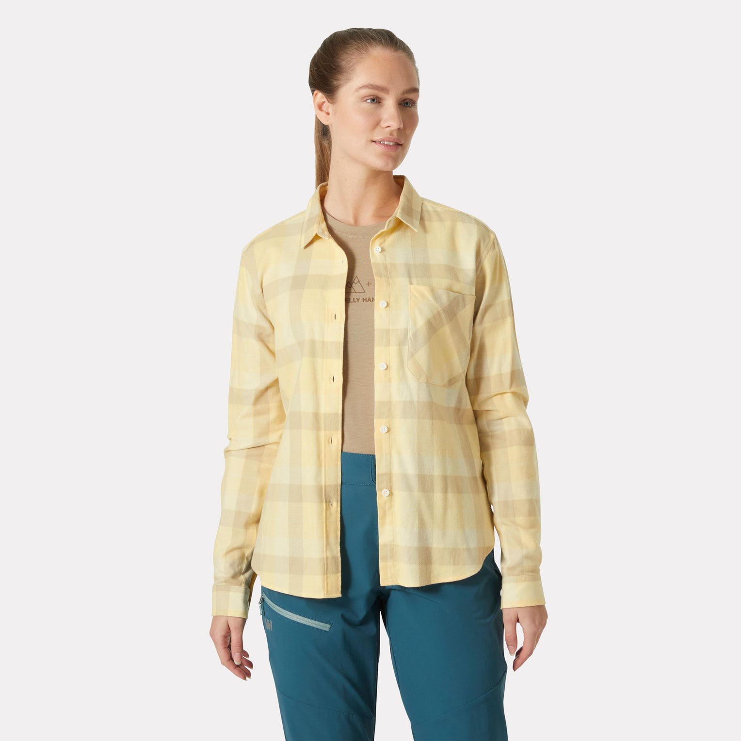 Yellow plaid long sleeve shirt by Helly Hansen, featuring a button-up front, chest pocket, and a relaxed fit, paired with a beige top and teal pants.