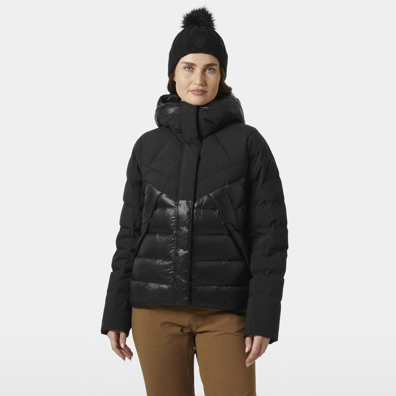 Black women's down jacket with a glossy front panel, featuring a high collar, hood, and quilted design, paired with a black beanie and brown pants.