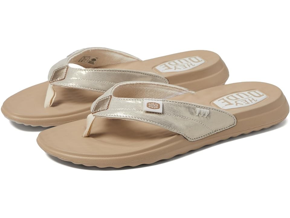 Gold flip-flop sandals featuring a metallic strap, cushioned beige sole, and HEYDUDE logo detail, ideal for casual summer wear.