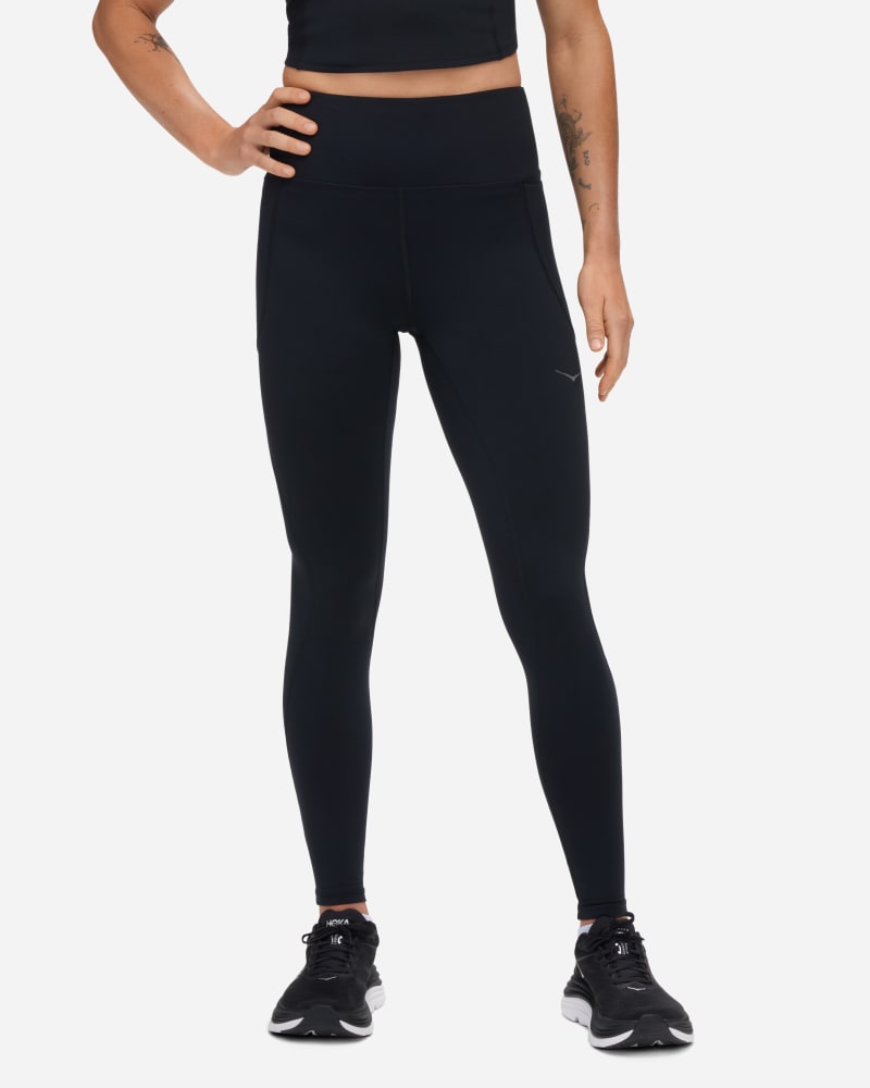 Black HOKA Women's Elaro Knit Tight 27" in size small, featuring a high waistband, stretchy knit material, and a sleek, form-fitting design, paired with black athletic shoes.