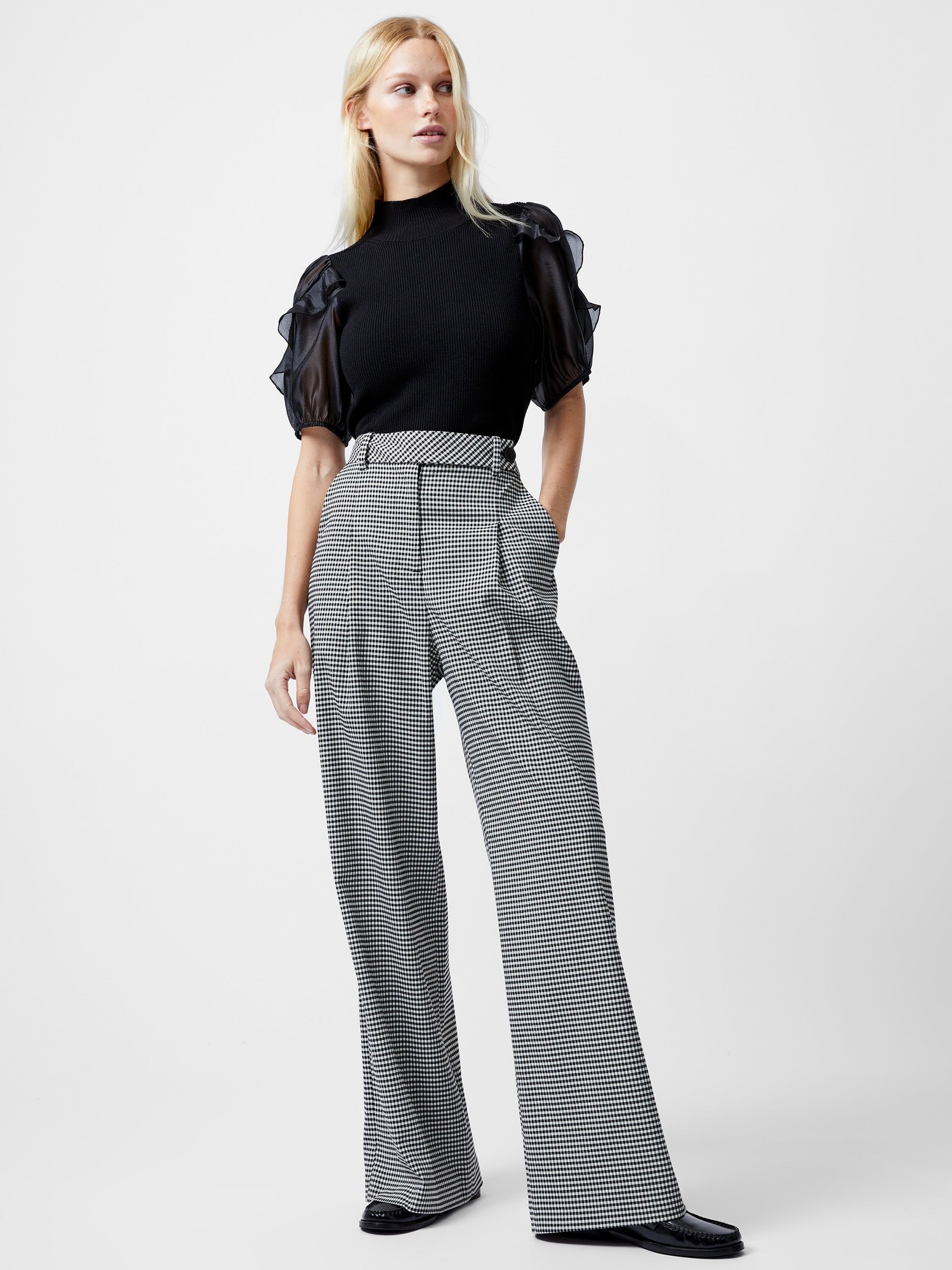 Black and ecru houndstooth trousers with a high waist, wide-leg fit, and front pockets, styled with a black top featuring sheer puff sleeves.