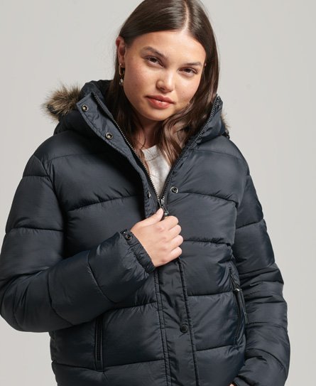 Navy hooded puffer jacket by Superdry, featuring a faux fur trim on the hood, zip and button closure, and quilted design, worn by a model with long hair.