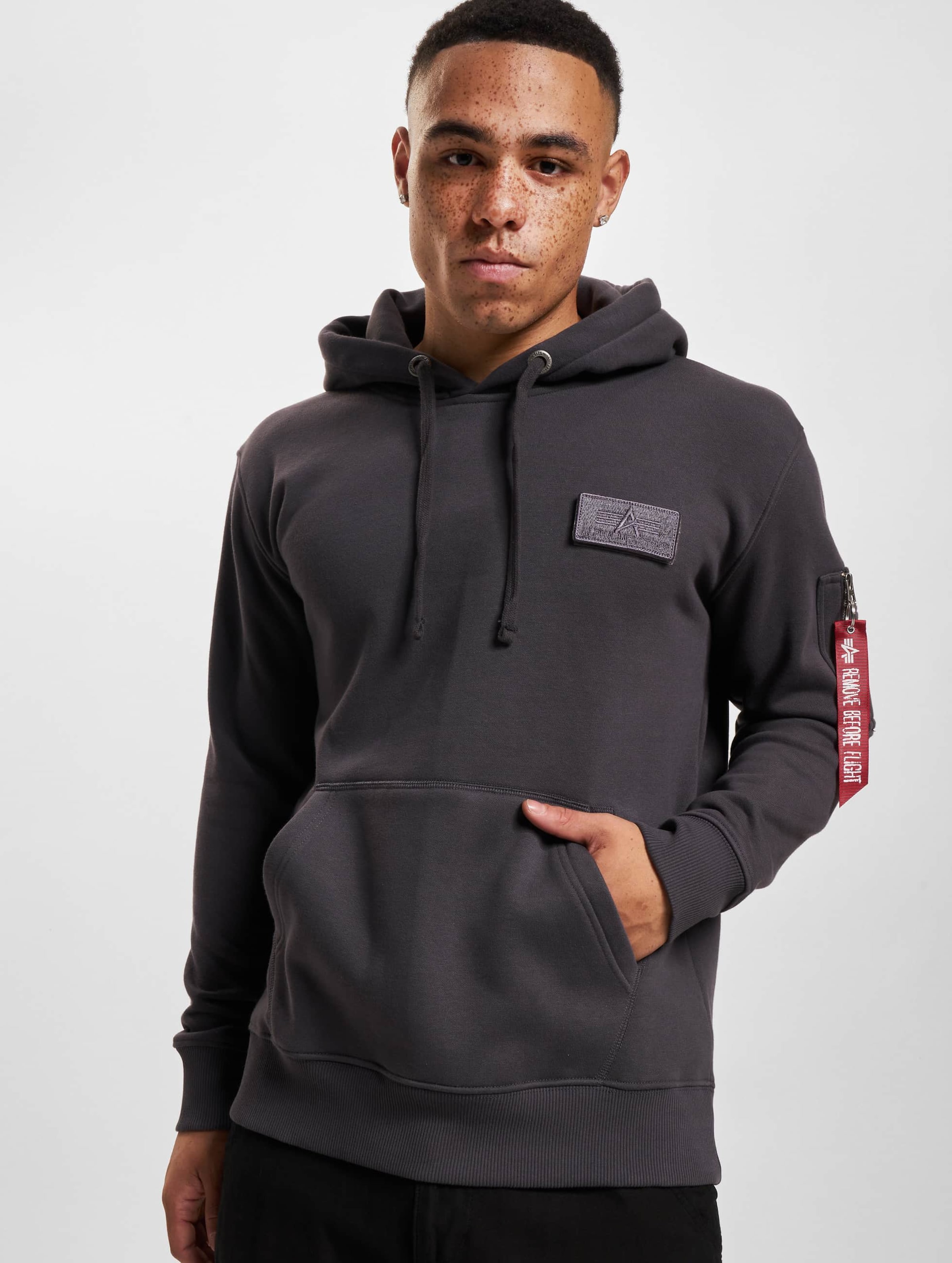 Gray hooded sweatshirt featuring a front kangaroo pocket, a patch on the chest, and a signature red tag on the sleeve, made from soft, comfortable material.