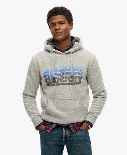 Light gray hooded sweatshirt featuring a stacked Superdry logo in blue and black, made from soft material, with a front pocket and drawstring hood, worn over a plaid shirt.