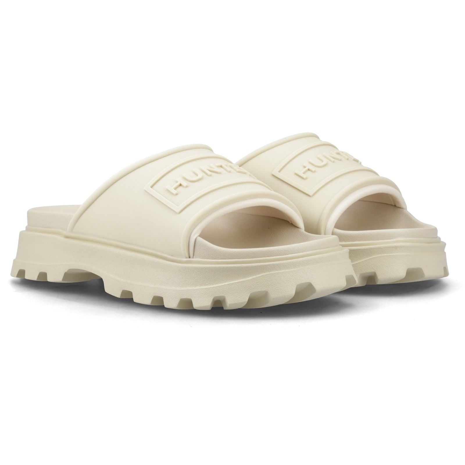 Cream-colored molded polyester slides with a thick, textured sole and a wide strap featuring the embossed "Hunter" logo.