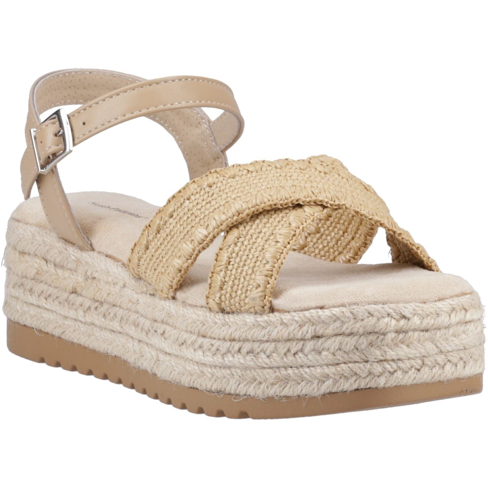 Tan polyurethane sandals with cross-strap design, woven jute detailing, and a thick espadrille sole, featuring an adjustable ankle strap for a secure fit.