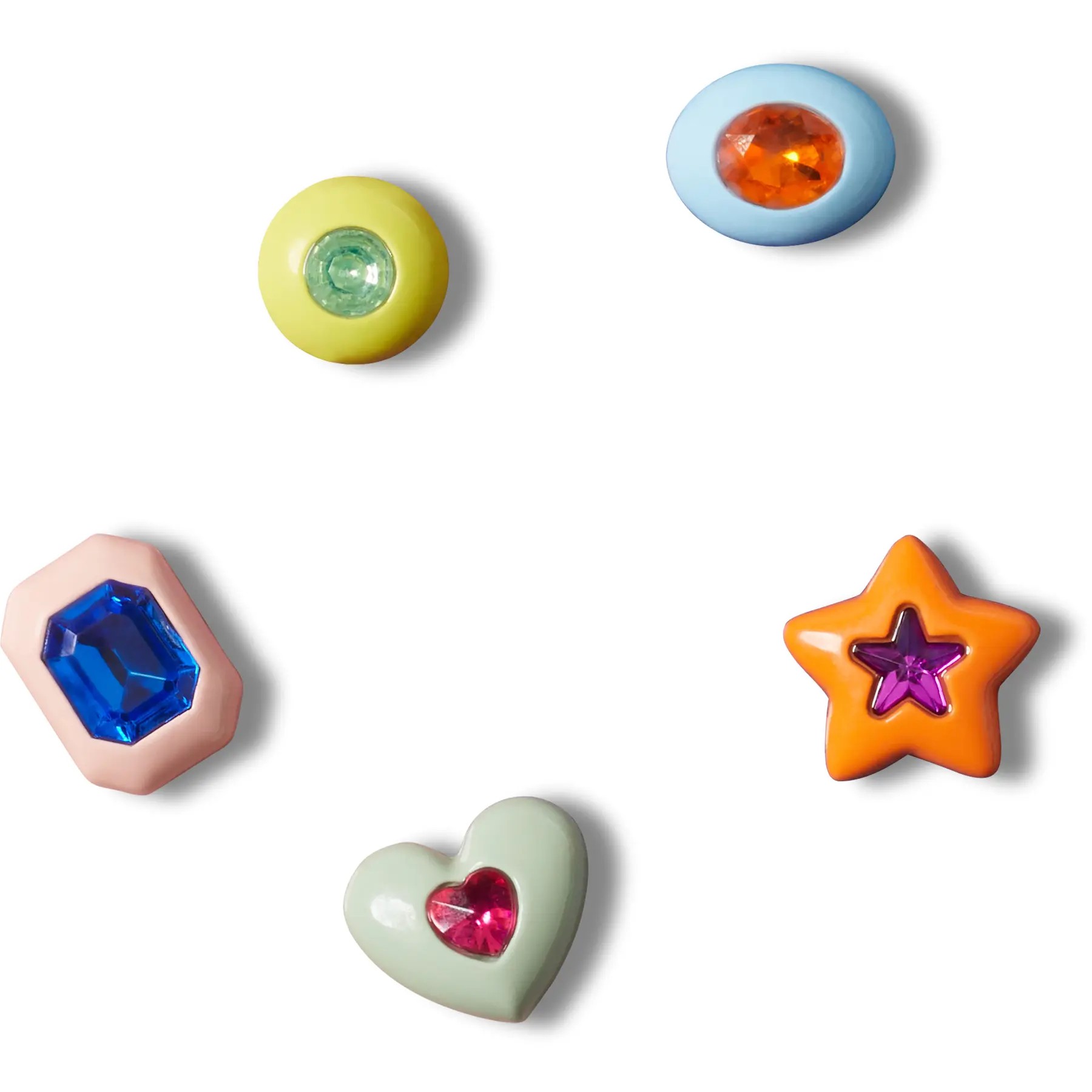Five colorful Jibbitz charms for Crocs, featuring a yellow gem, a blue oval with an orange gem, a pink heart with a red gem, a green star with a purple gem, and a blue diamond shape.