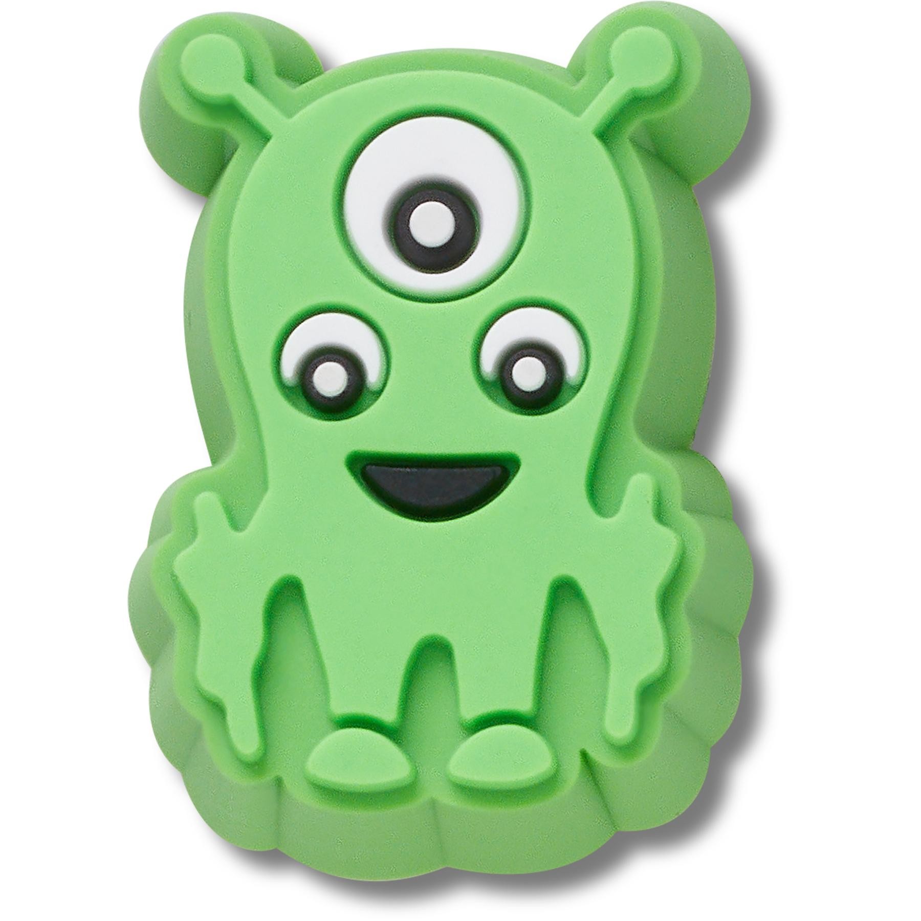 Tiny green monster-shaped Jibbitz charm for Crocs, featuring a smiling face, three eyes, and two antennae, made of soft rubber material with a textured finish.