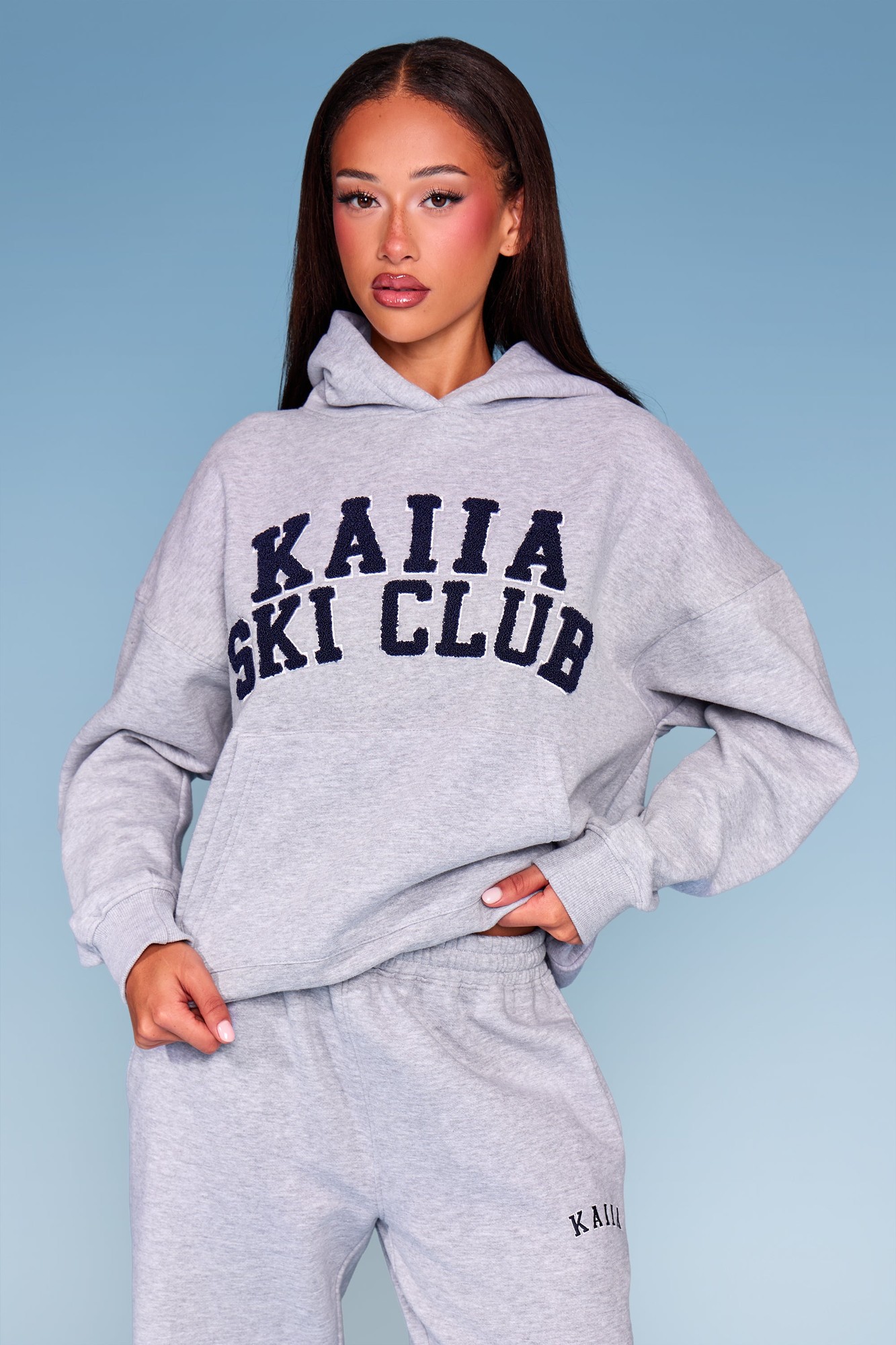 Oversized mid-grey marl hoodie featuring "KAIIA SKI CLUB" in navy lettering, with a relaxed fit and a hood, paired with matching sweatpants.
