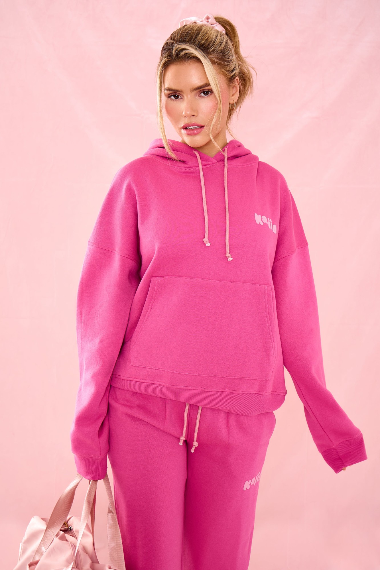 Oversized hoodie in vibrant dragonfruit pink, featuring a kangaroo pocket and drawstring hood, paired with matching sweatpants, creating a stylish, cozy look.