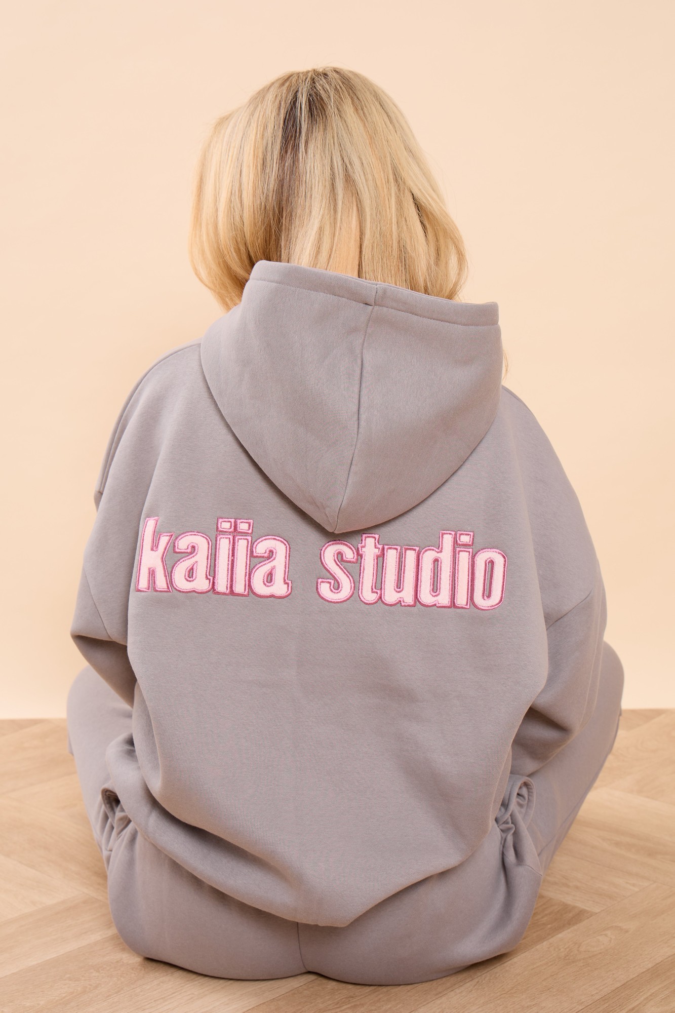 Oversized hoodie in earl grey with a pink "kaiia studio" logo on the back, featuring a cozy hood and relaxed fit, styled with a soft, comfortable material.