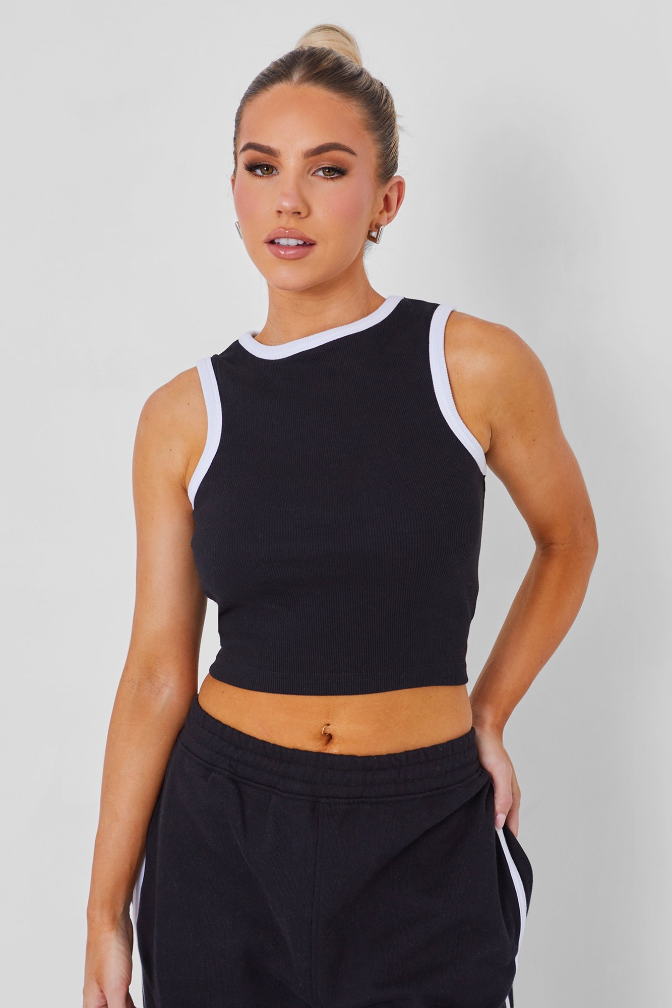 Black ribbed vest with white contrast binding along the neckline and armholes, featuring a cropped fit and worn with black sweatpants.