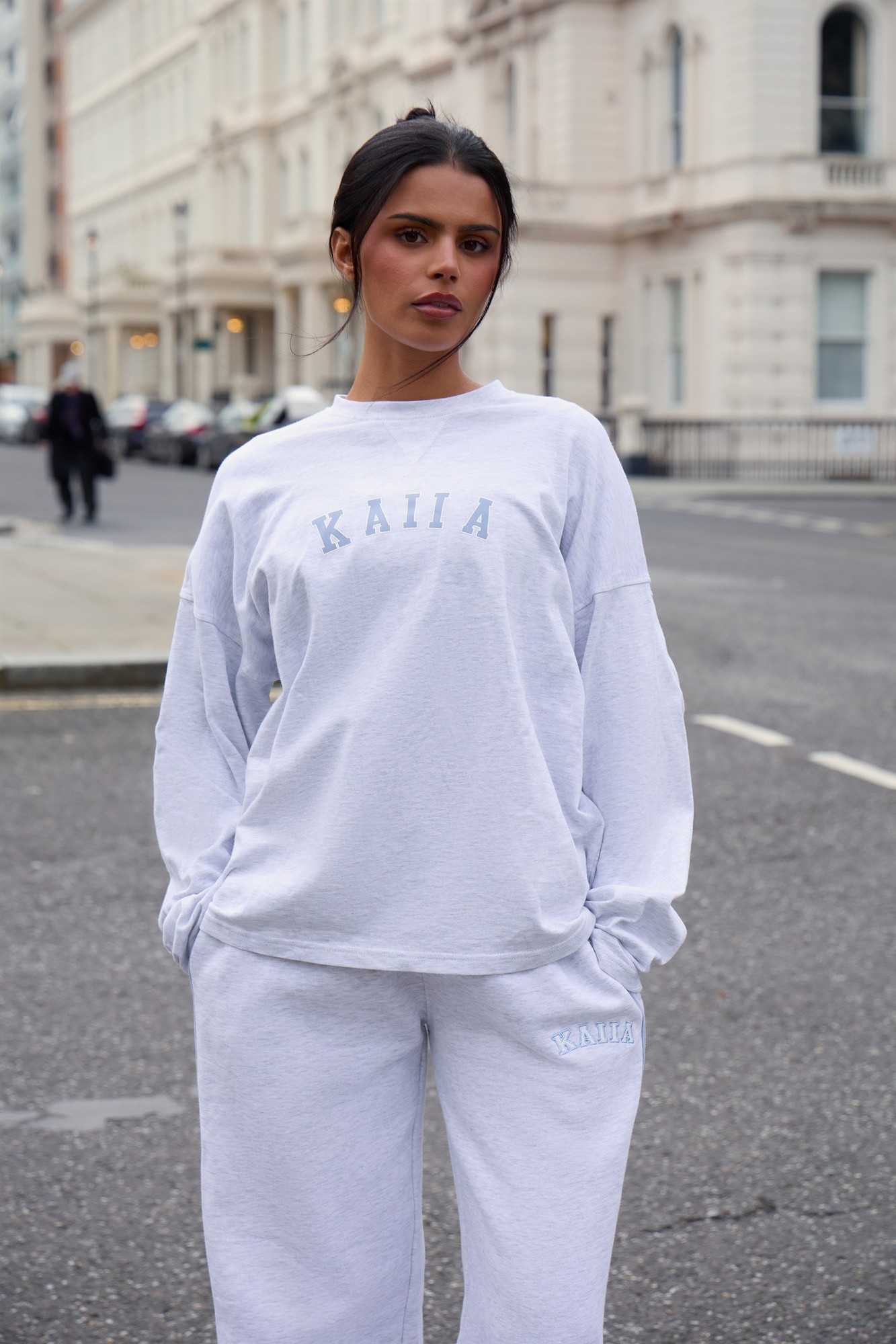 Light grey marl oversized long sleeve T-shirt with "KAIIA" printed in light blue, styled with matching sweatpants, worn by a model in an urban setting.
