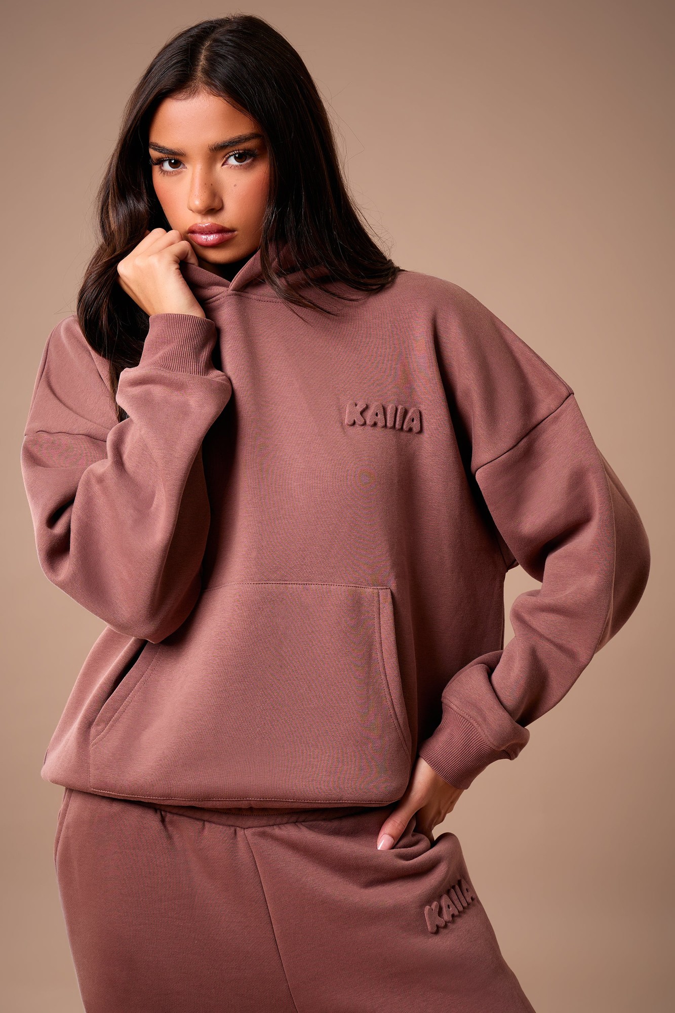 Oversized nutmeg hoodie featuring an embossed "Kaiia" logo on the chest, made from soft, cozy material, styled with a front pocket and relaxed fit.