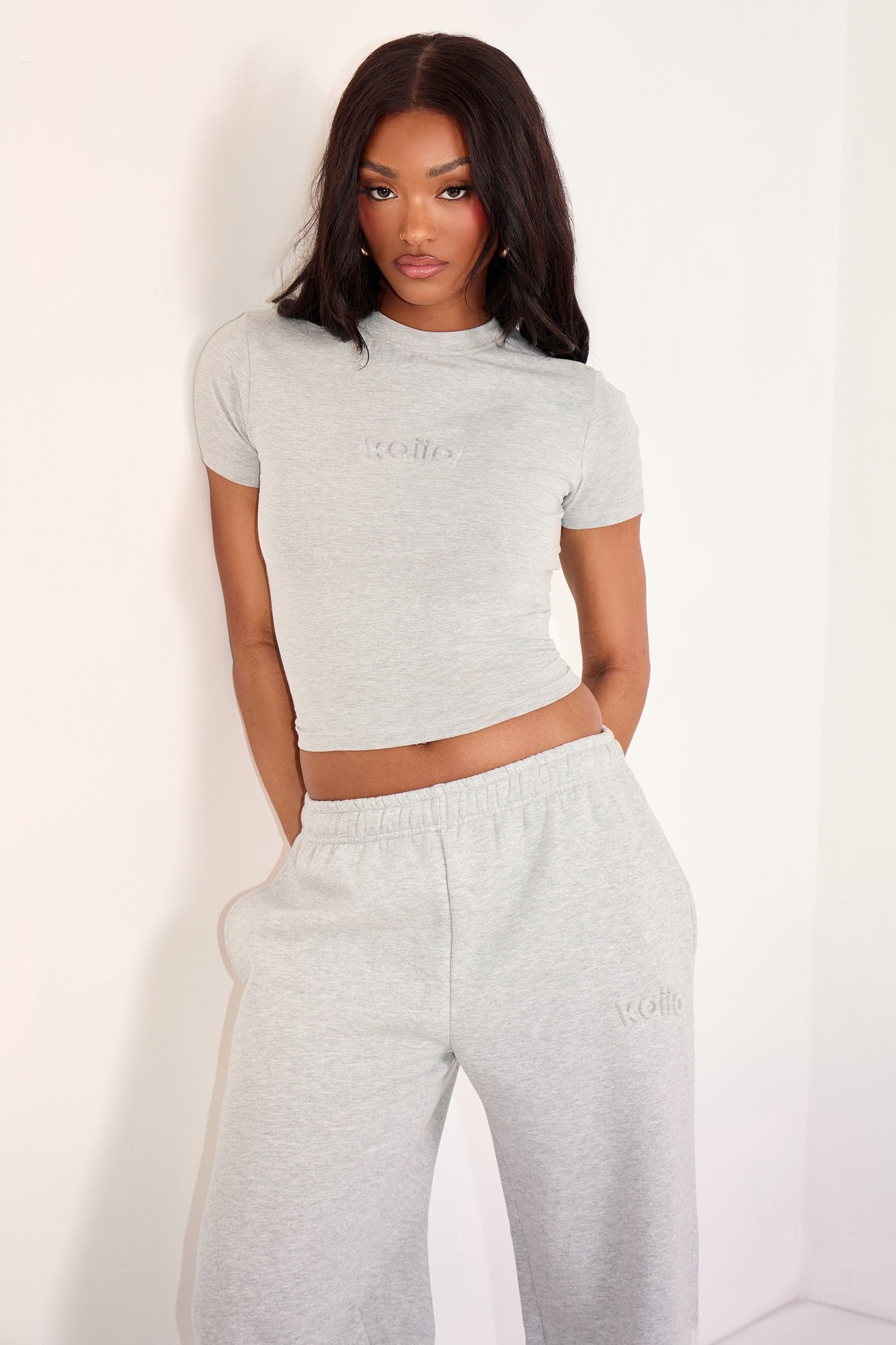 Mid grey marl baby tee featuring an embossed logo, short sleeves, and a fitted silhouette, paired with matching grey sweatpants for a coordinated look.