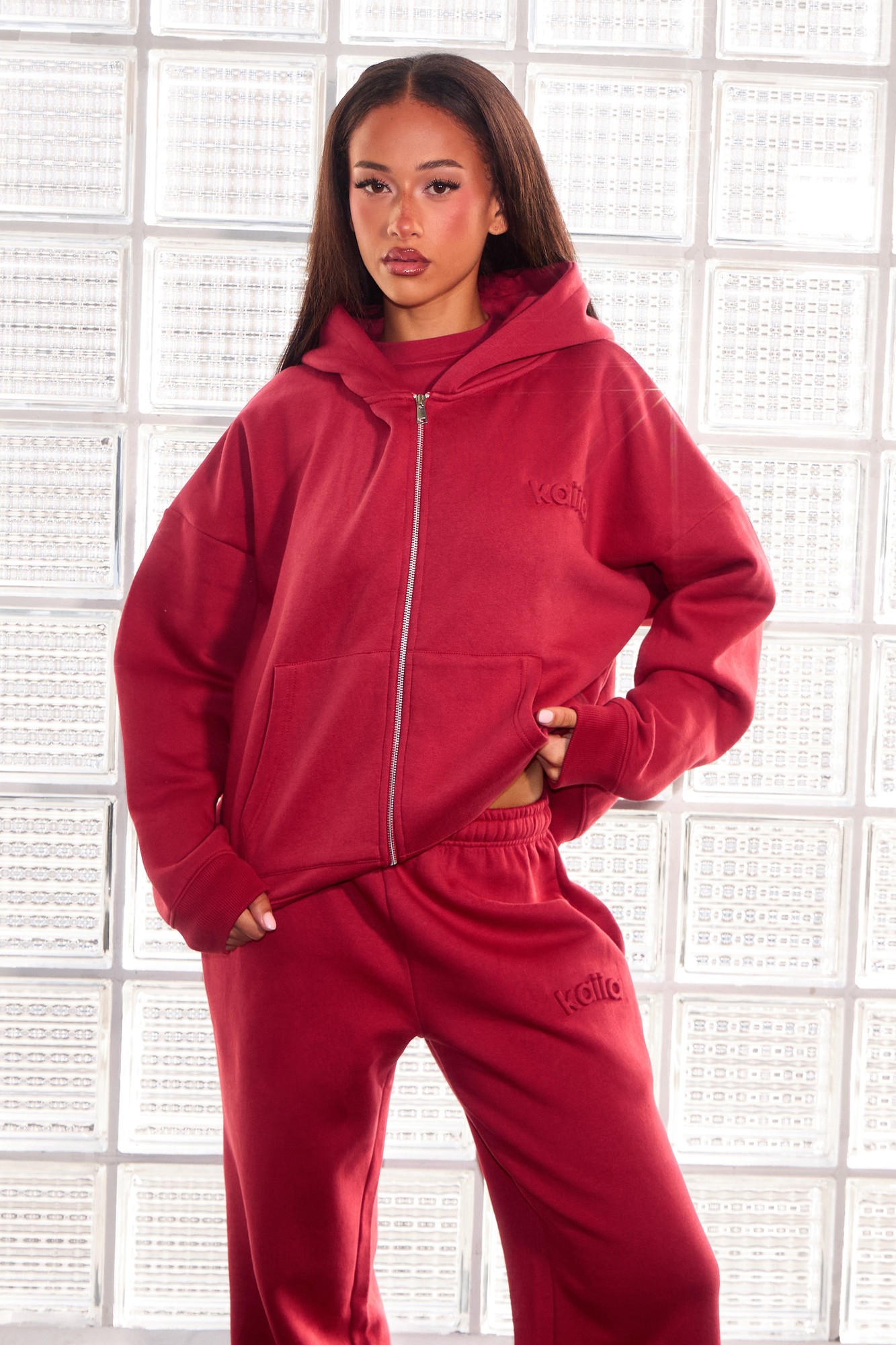 Oversized deep red zip-through hoodie with embossed logo, featuring a spacious hood and front pockets, styled with matching sweatpants.
