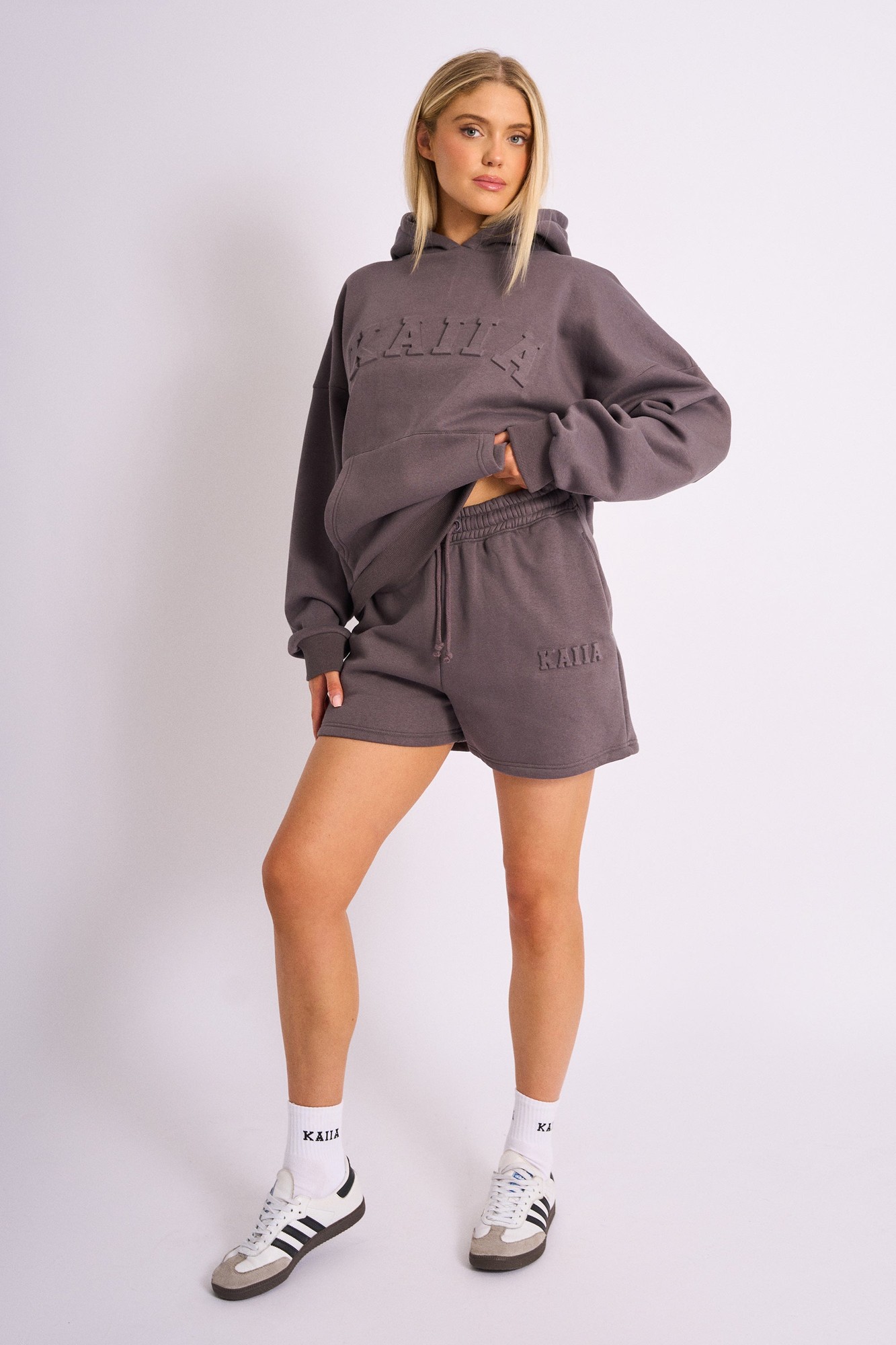 Dark grey sweat shorts featuring an embossed "Kaiia" logo on the front, made from soft material, styled with a drawstring waist and paired with a matching hoodie.