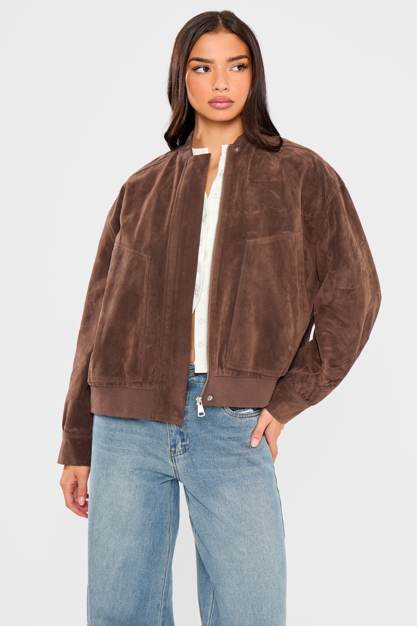Brown faux suede bomber jacket featuring a zip closure, two front pockets, and a relaxed fit, styled with a white shirt and blue jeans.