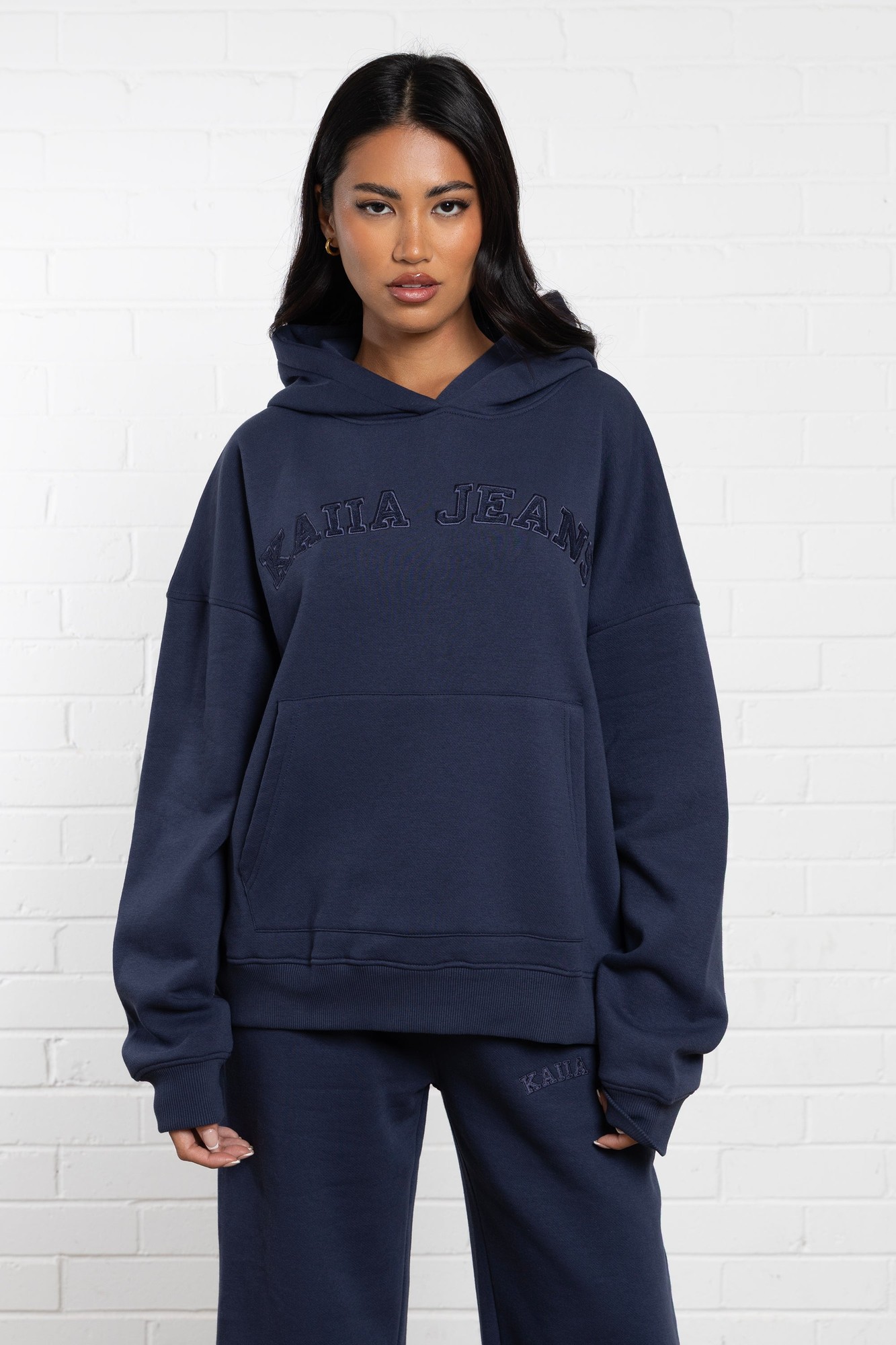 Oversized indigo hoodie by Kaiia, featuring a front kangaroo pocket, embroidered "Kaiia Jeans" logo, and a cozy, soft material, styled with matching pants.