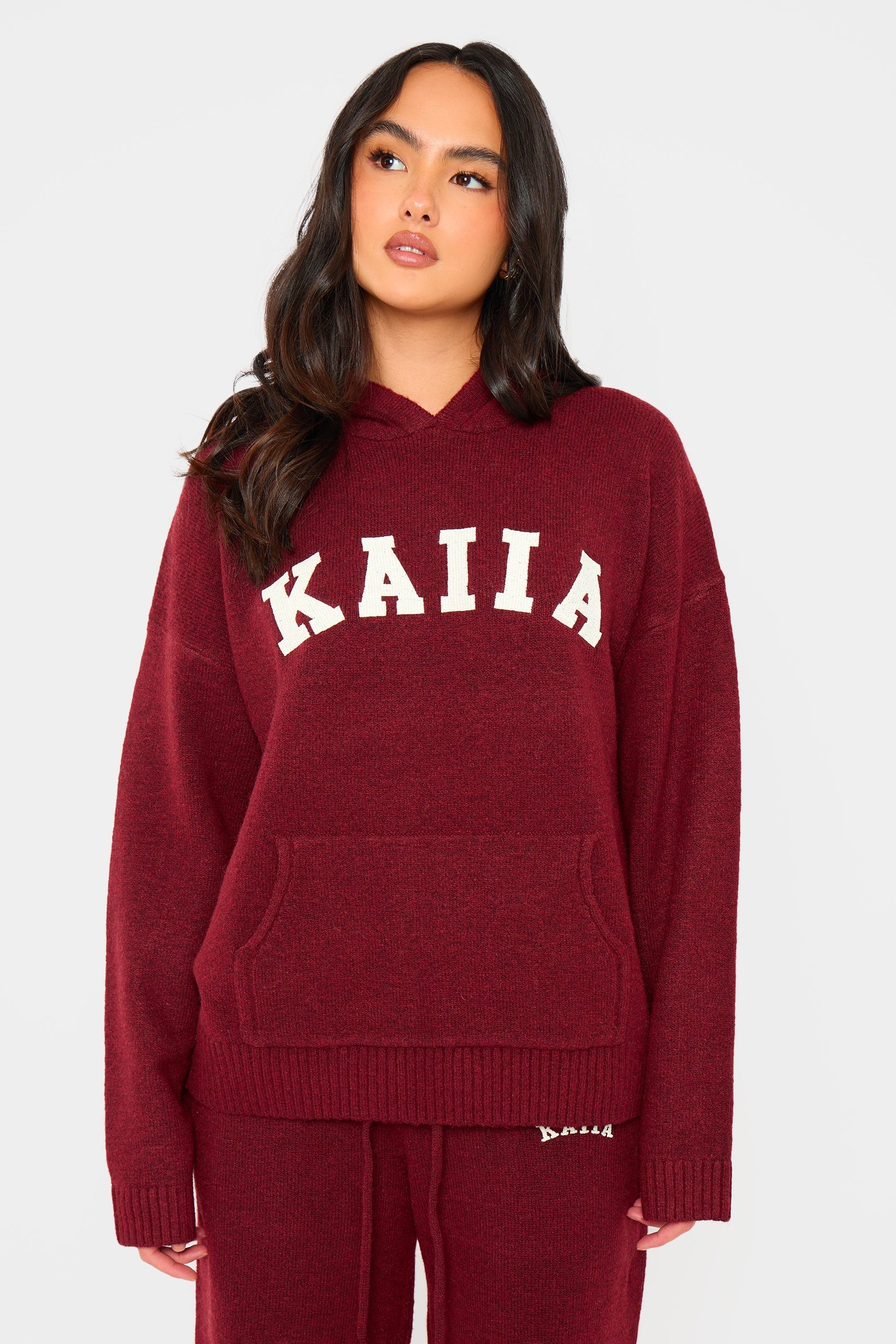 Burgundy oversized knit hoodie featuring a front pocket and "KAIIA" in cream letters across the chest, made from soft, cozy material.