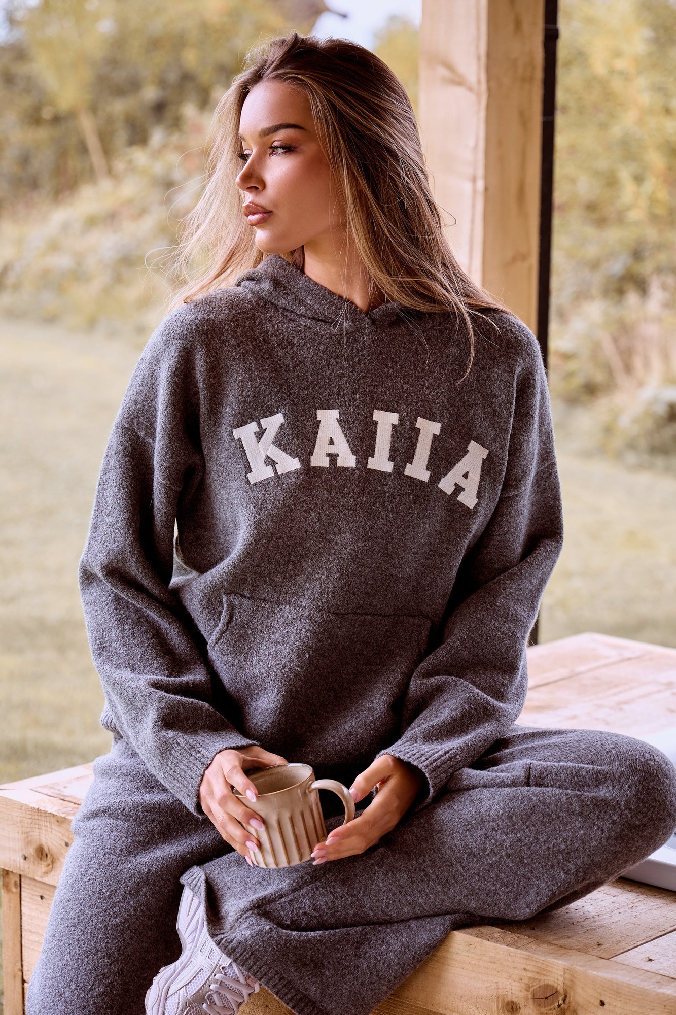 Charcoal oversized hoodie made of soft knit fabric, featuring a front pocket and "KAIIA" lettering in white across the chest, styled with relaxed-fit pants.